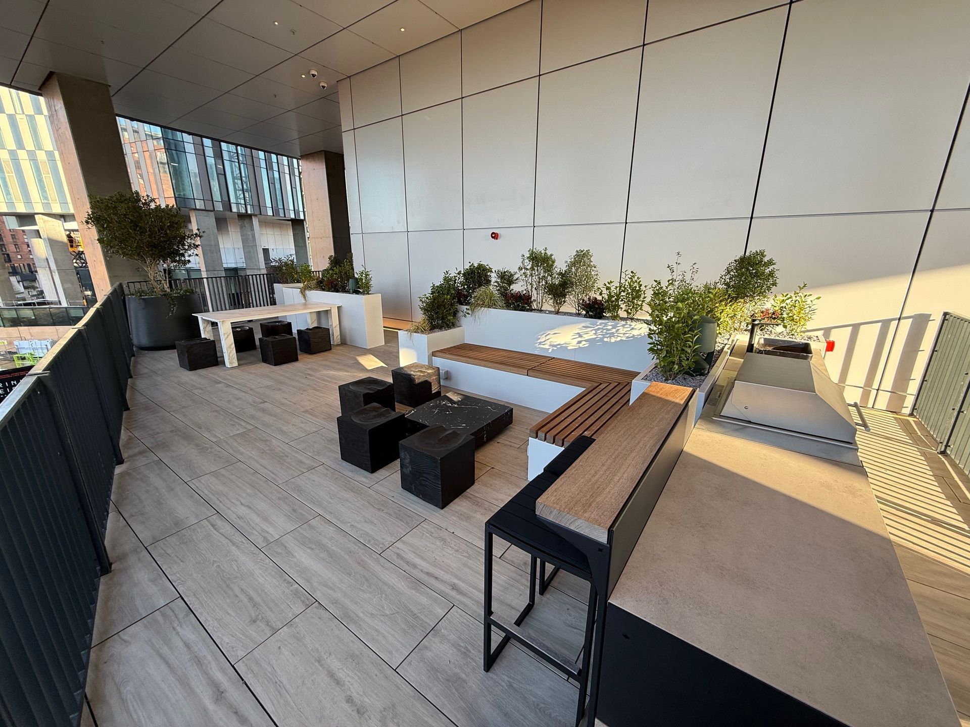 Rooftop patio with white and wooden furniture, plants, and a cityscape view.