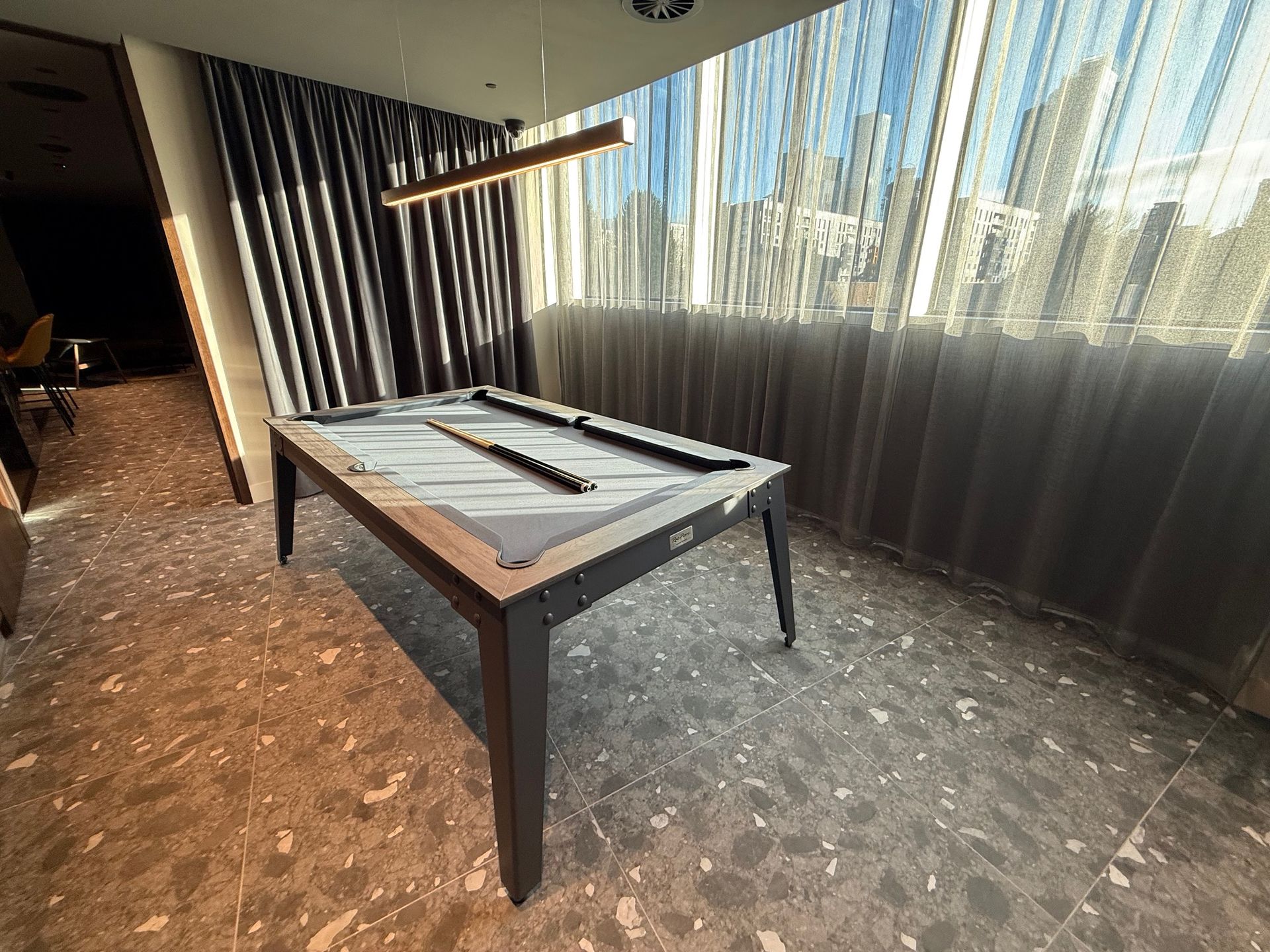 Pool table in room with sunlight, next to curtains and window.