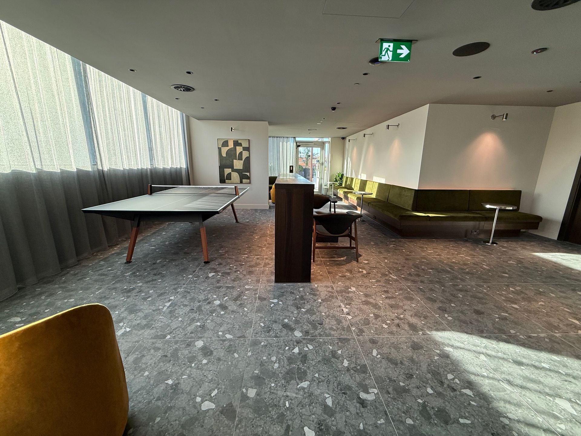 Lobby with a ping pong table, green couch, and speckled gray floor; large window on left.