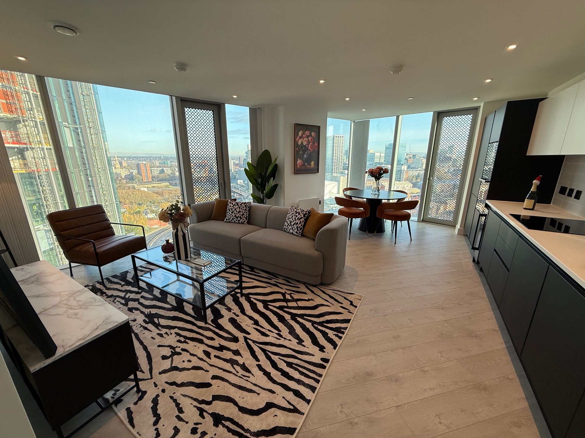 Modern living room with city view, zebra rug, grey sofa, brown armchair, and black cabinets.