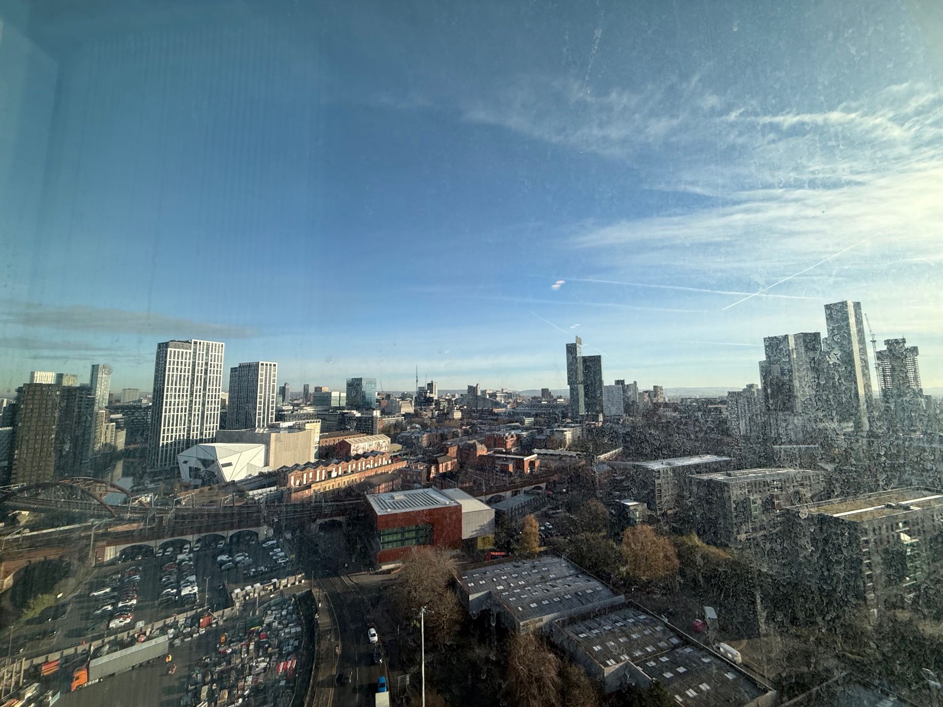 City skyline under a blue sky, viewed from a high angle. Buildings of various heights and styles.