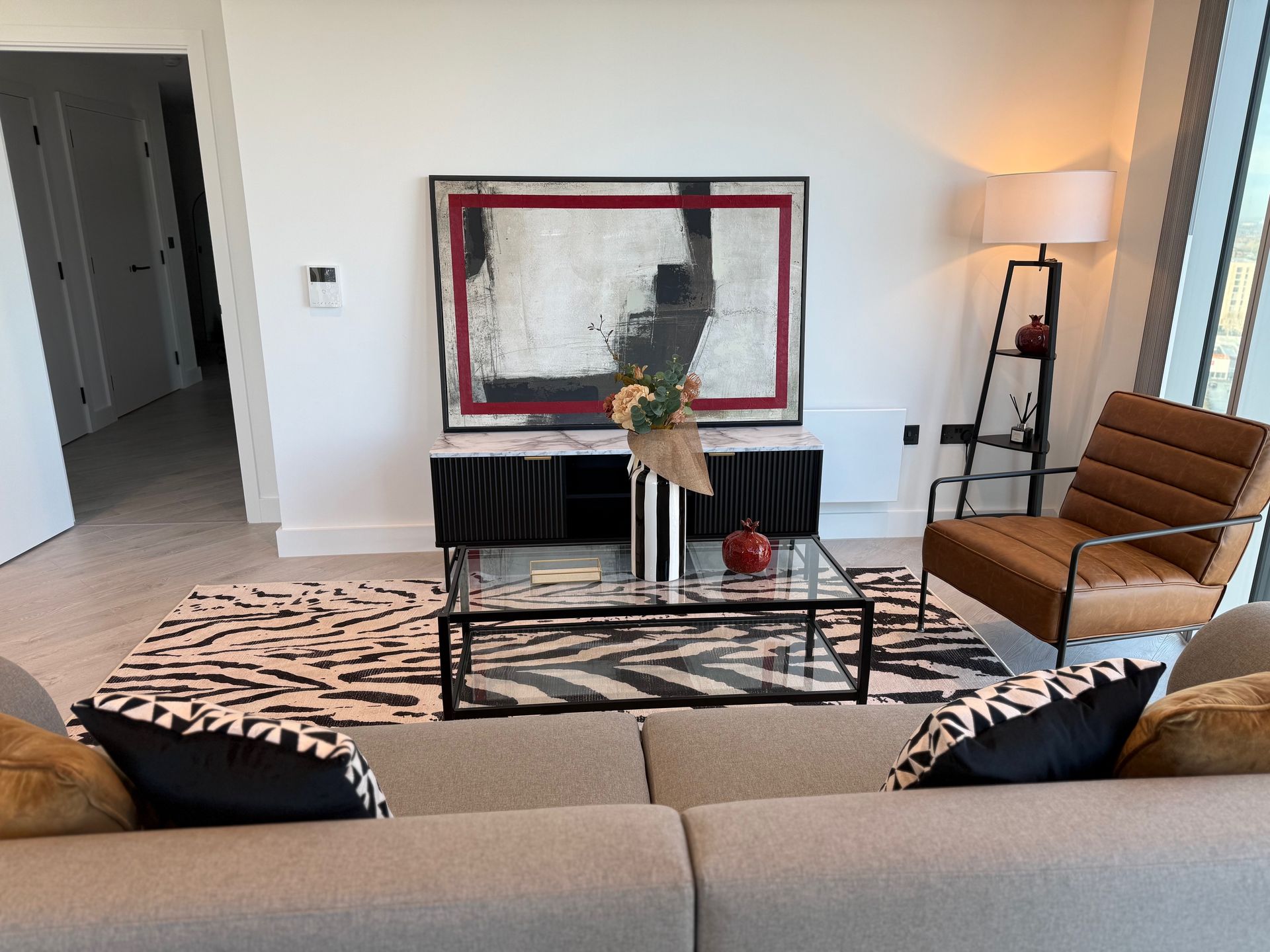 Living room with modern decor; abstract painting, zebra rug, leather chair, and neutral-toned couch.