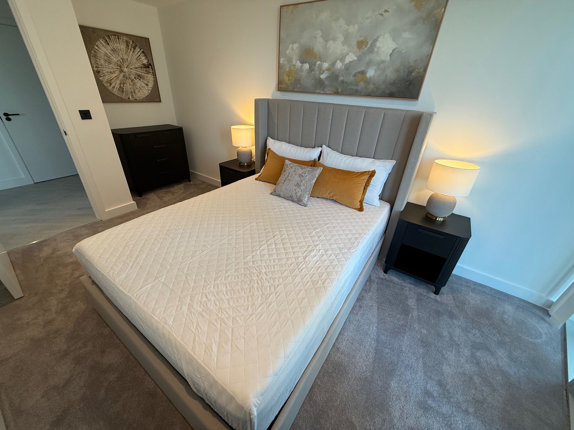 Bedroom with bed, nightstands, lamps, artwork, and gray carpet.