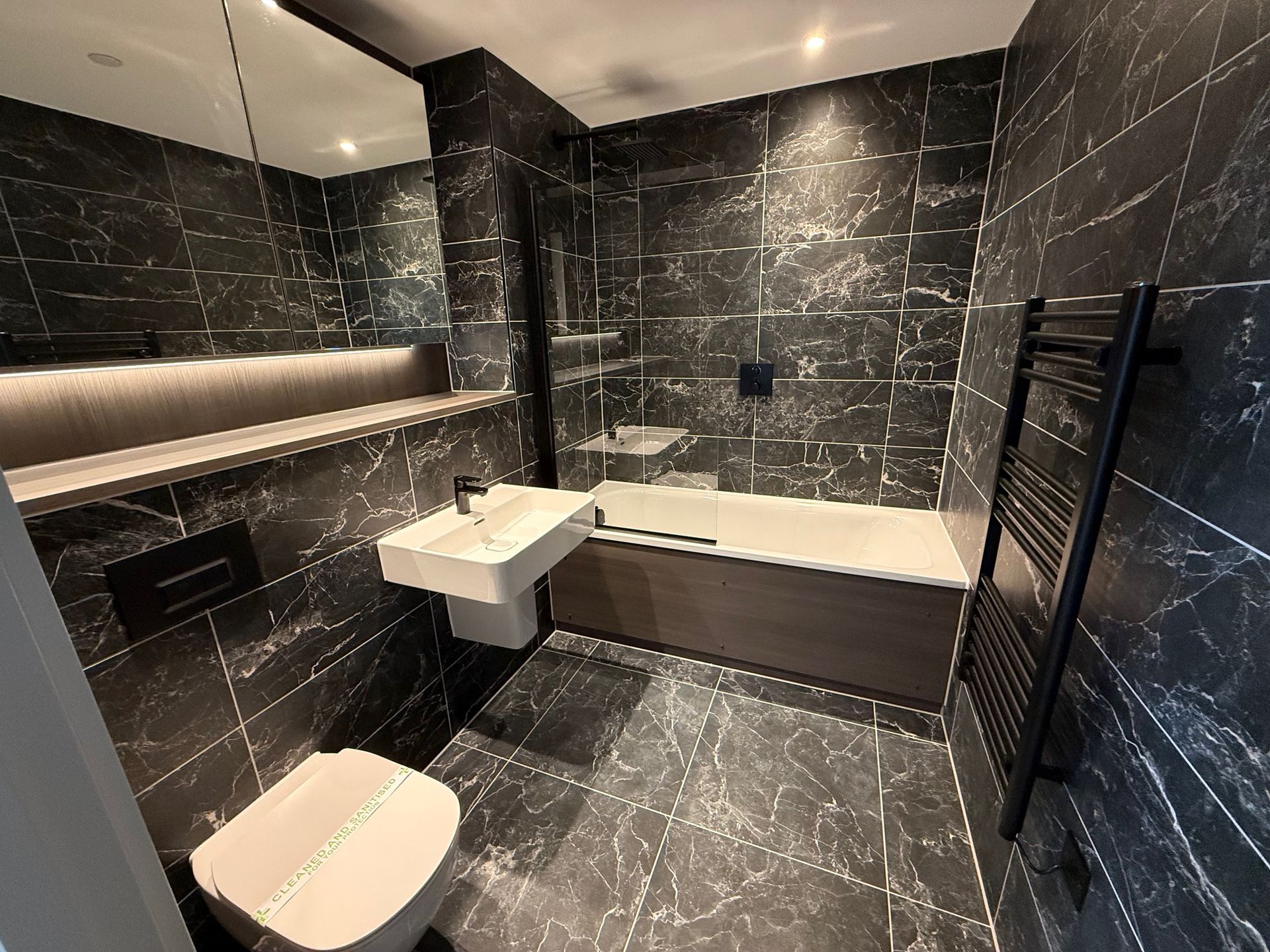 Modern bathroom with black marble tile, a wall-mounted toilet, and a bathtub with a towel rack.