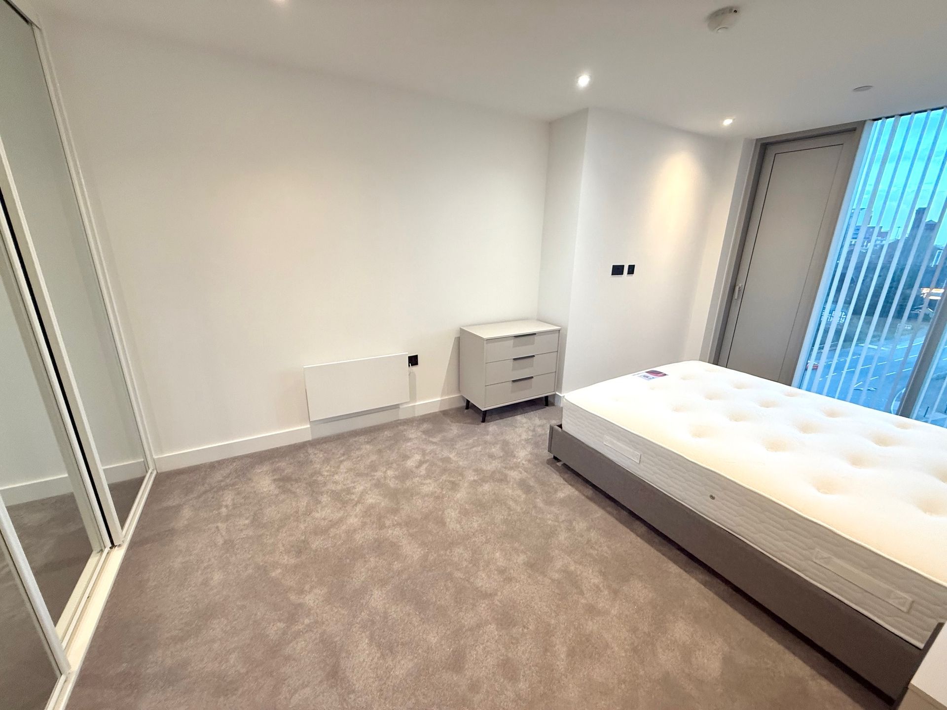 Bedroom with bed, dresser, built-in closet, and window. Gray carpet and white walls.