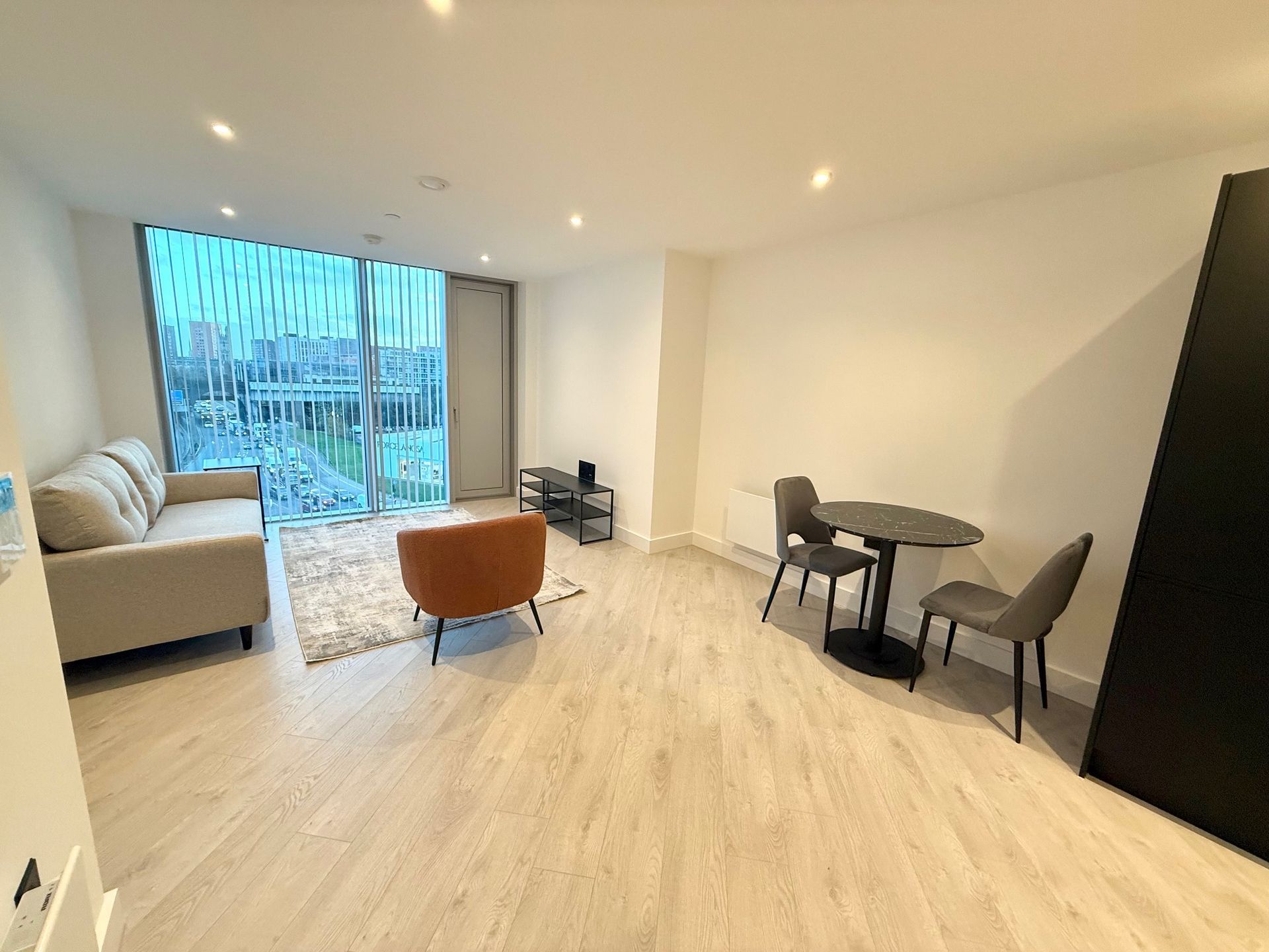 Living room with a sofa, armchair, table, chairs, and large window overlooking the city.