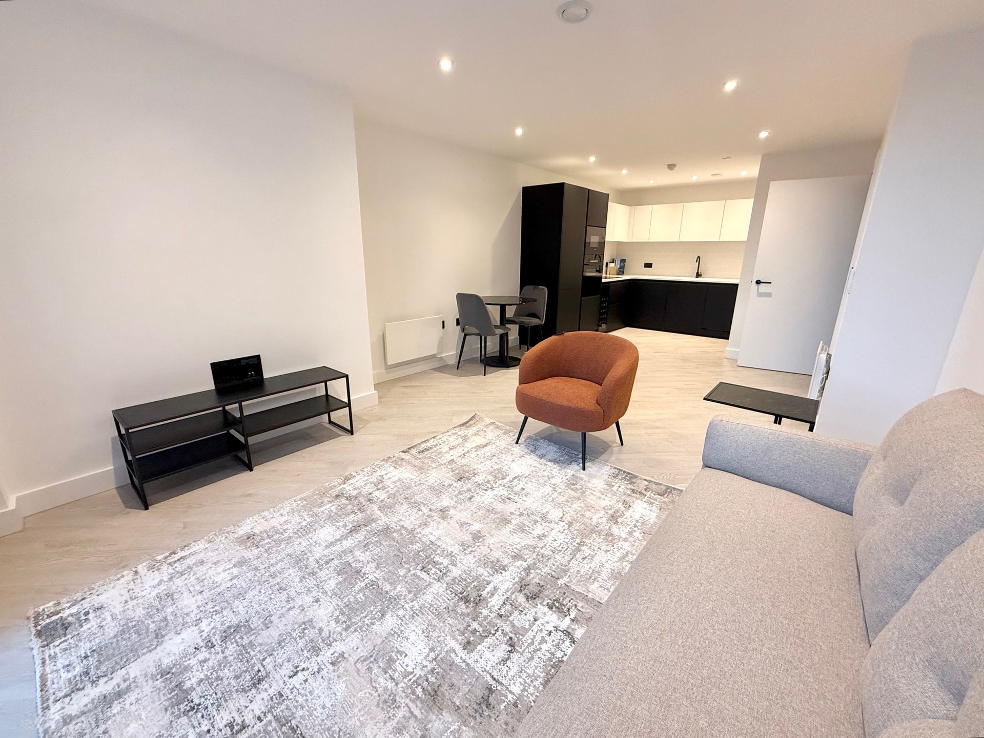 Modern living room with open kitchen. Includes sofa, armchair, rug, and TV stand.