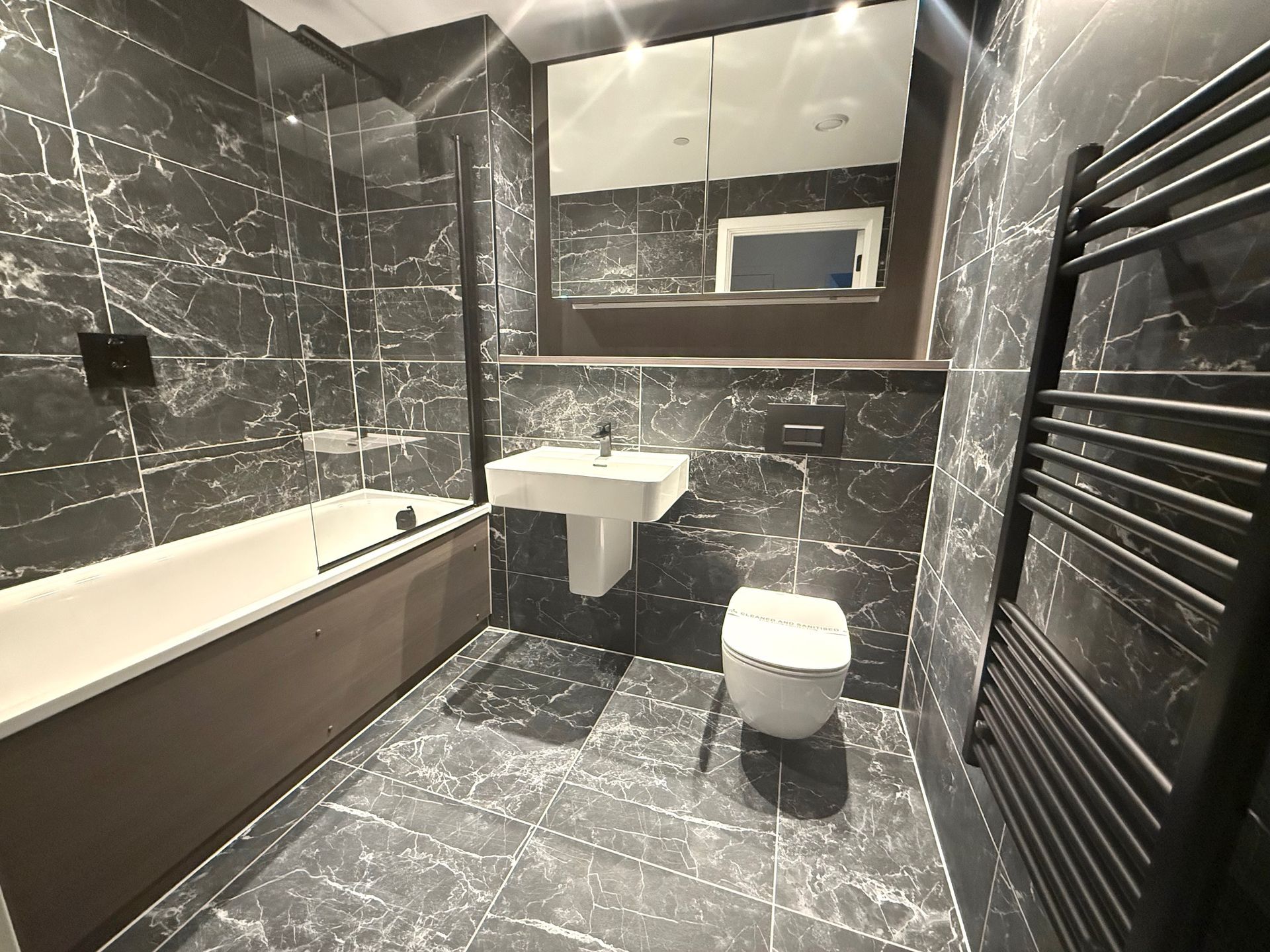 Modern bathroom with dark marble tile, bathtub, sink, toilet, and towel warmer.
