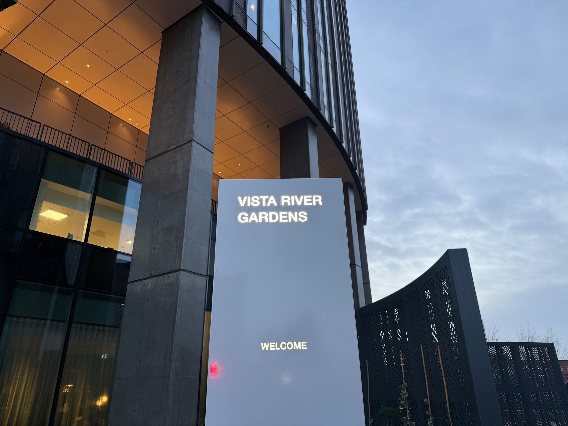 Sign for Vista River Gardens in front of a modern building, cloudy sky.