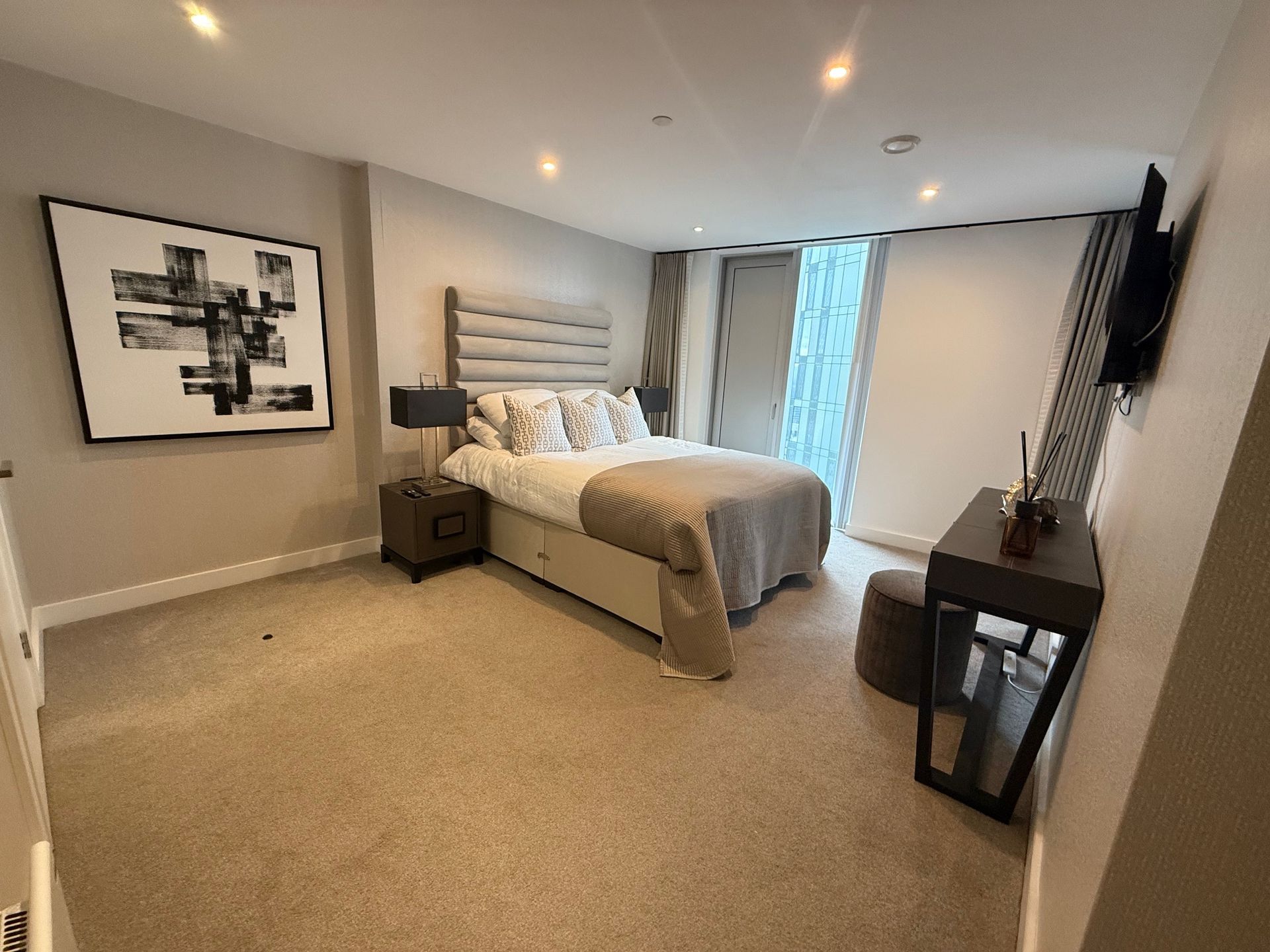 Bedroom with bed, nightstand, artwork, and desk. Beige carpet and neutral walls.