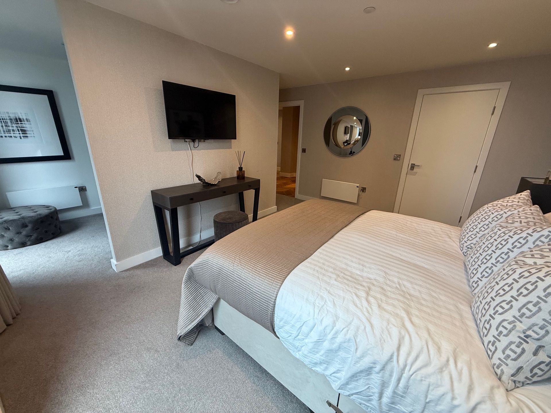 Bedroom with bed, TV, console table, and a framed print. Neutral color scheme, modern design.