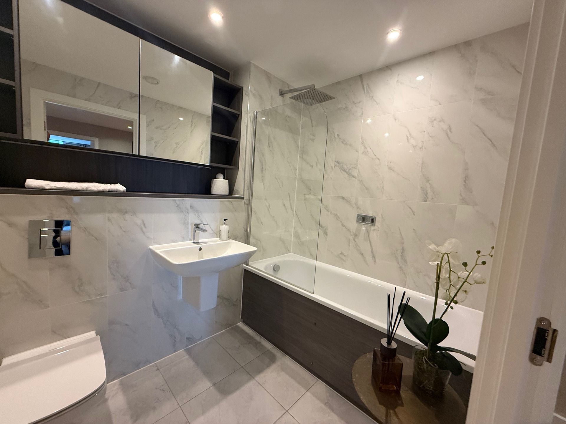 Modern bathroom with marble-look walls, a bathtub, sink, and toilet.