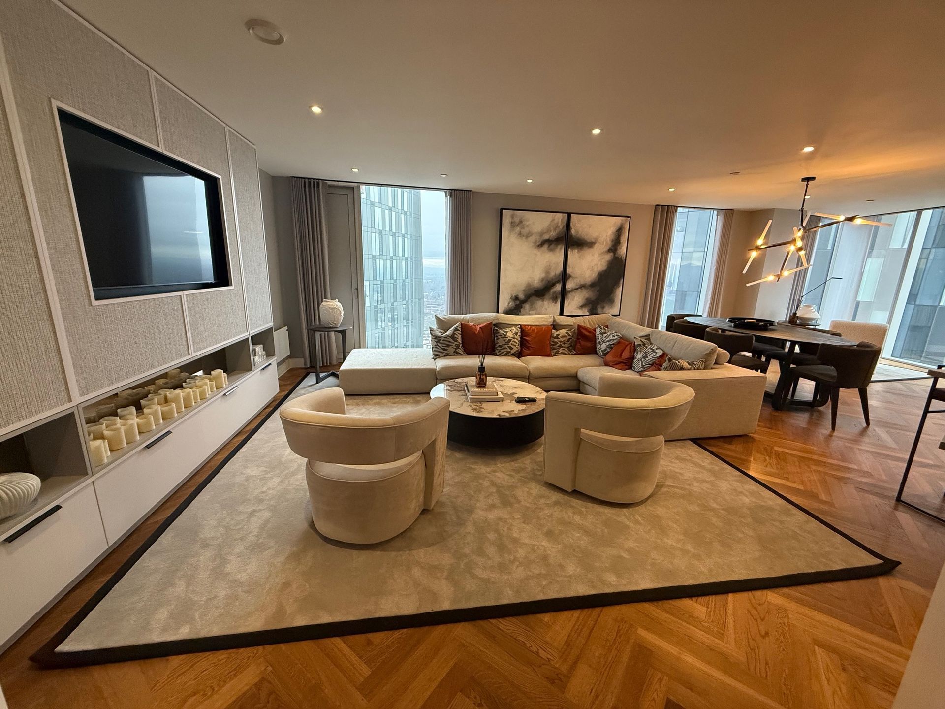 Luxurious living room with beige furniture, large TV, and city view.
