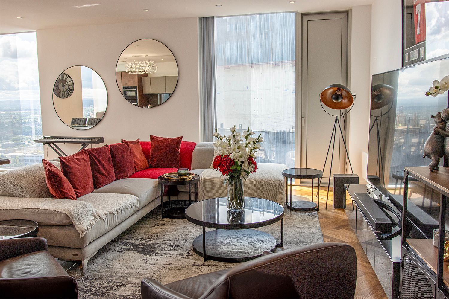 Living room with large sectional sofa, mirrors, and city view. Red and neutral tones.