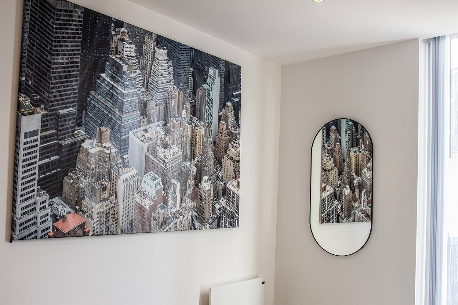 Large cityscape art and oval mirror on a white wall.