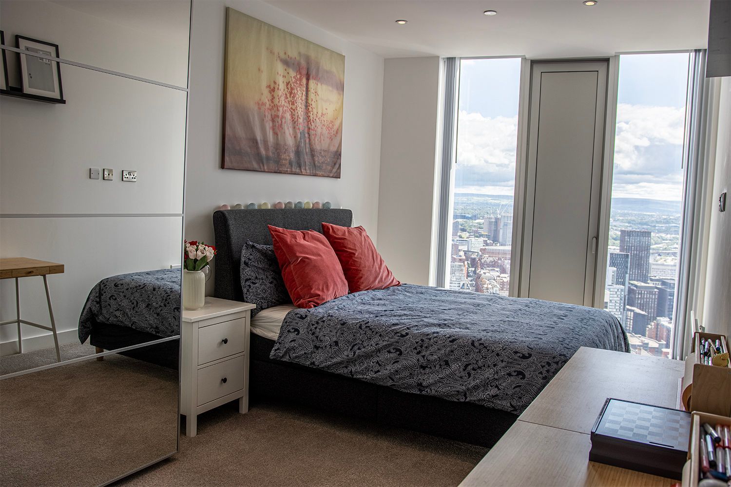 Bedroom with bed, large window, city view, and a mirrored wardrobe.