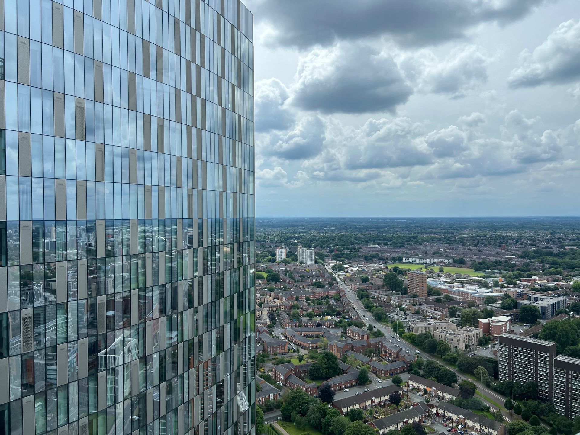 High-angle view of a glass skyscraper and a cityscape under a cloudy sky.