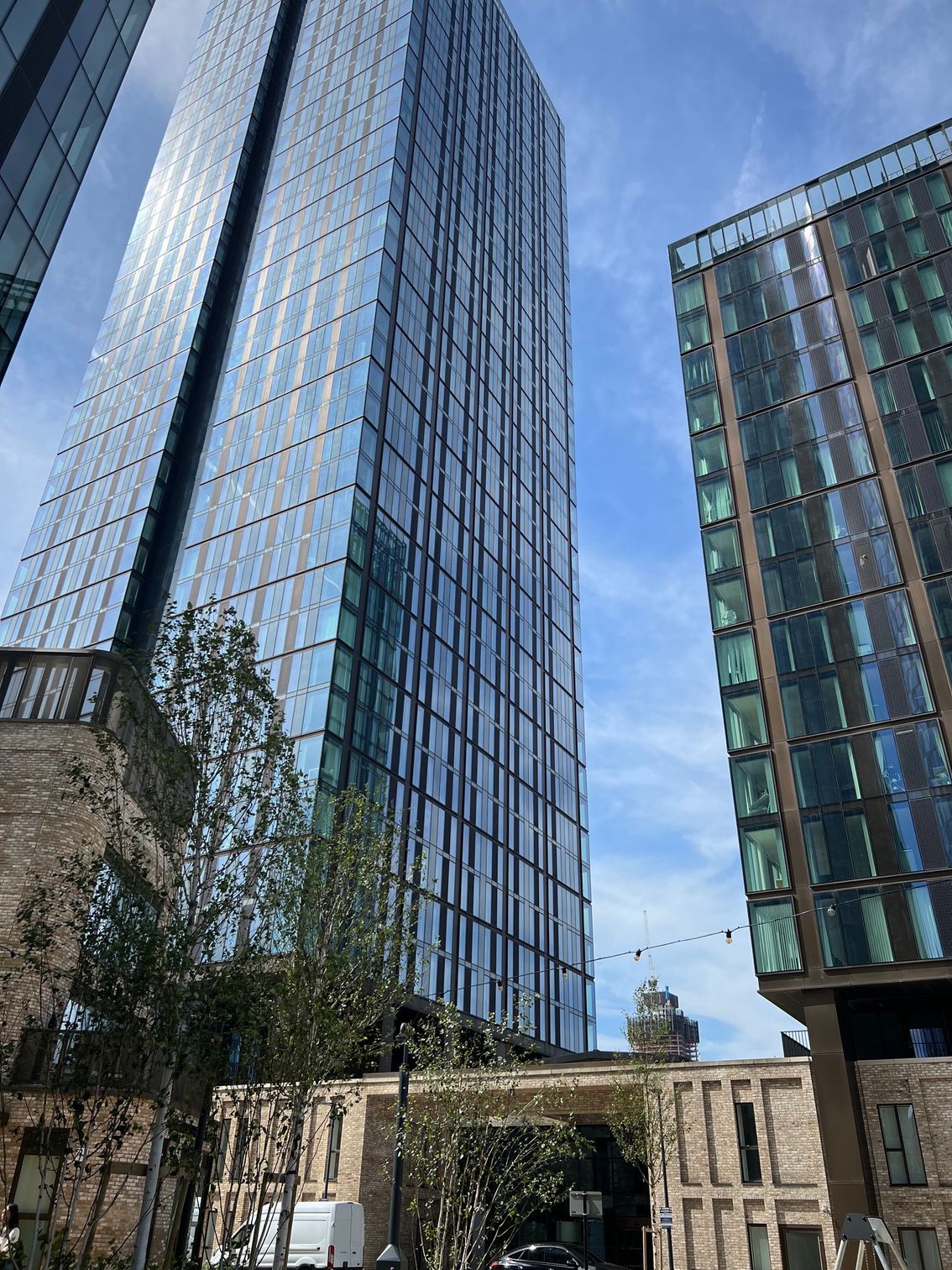 Two modern skyscrapers with glass facades against a blue sky, viewed from a brick-walled plaza.