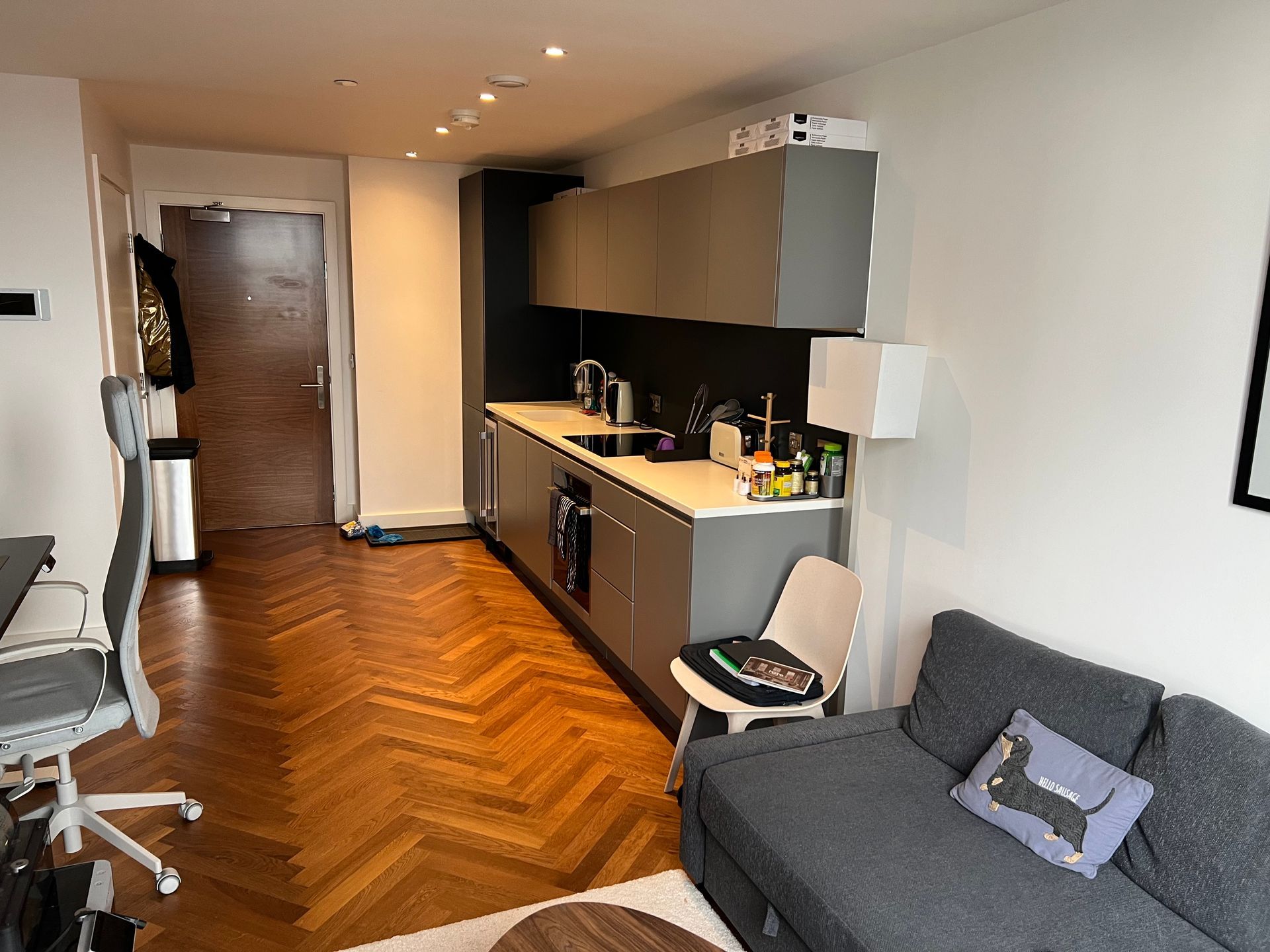 Small studio apartment with gray cabinets, kitchen, sofa, and wood floors.