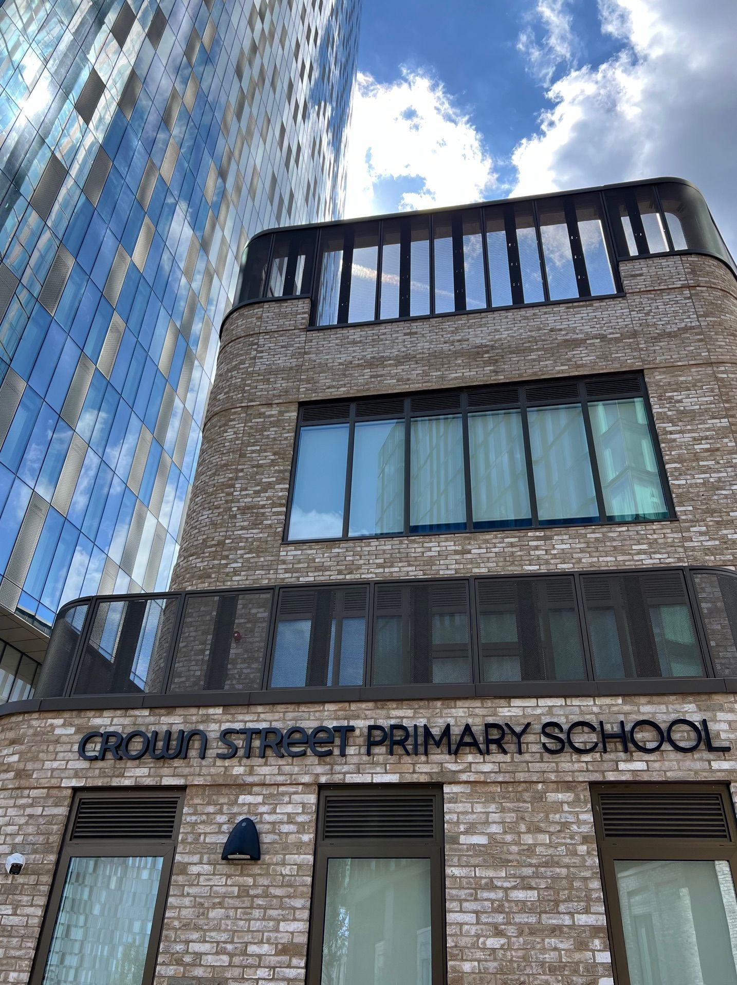 Crown Street Primary School building, brick facade, text over entrance, blue skyscraper background.