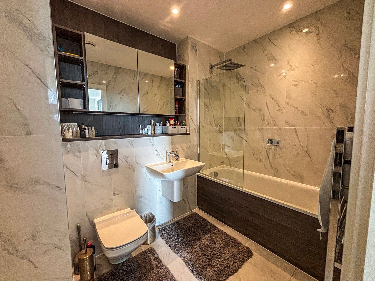 Modern bathroom with marble-look tile, a toilet, sink, tub, and mirrored medicine cabinet.