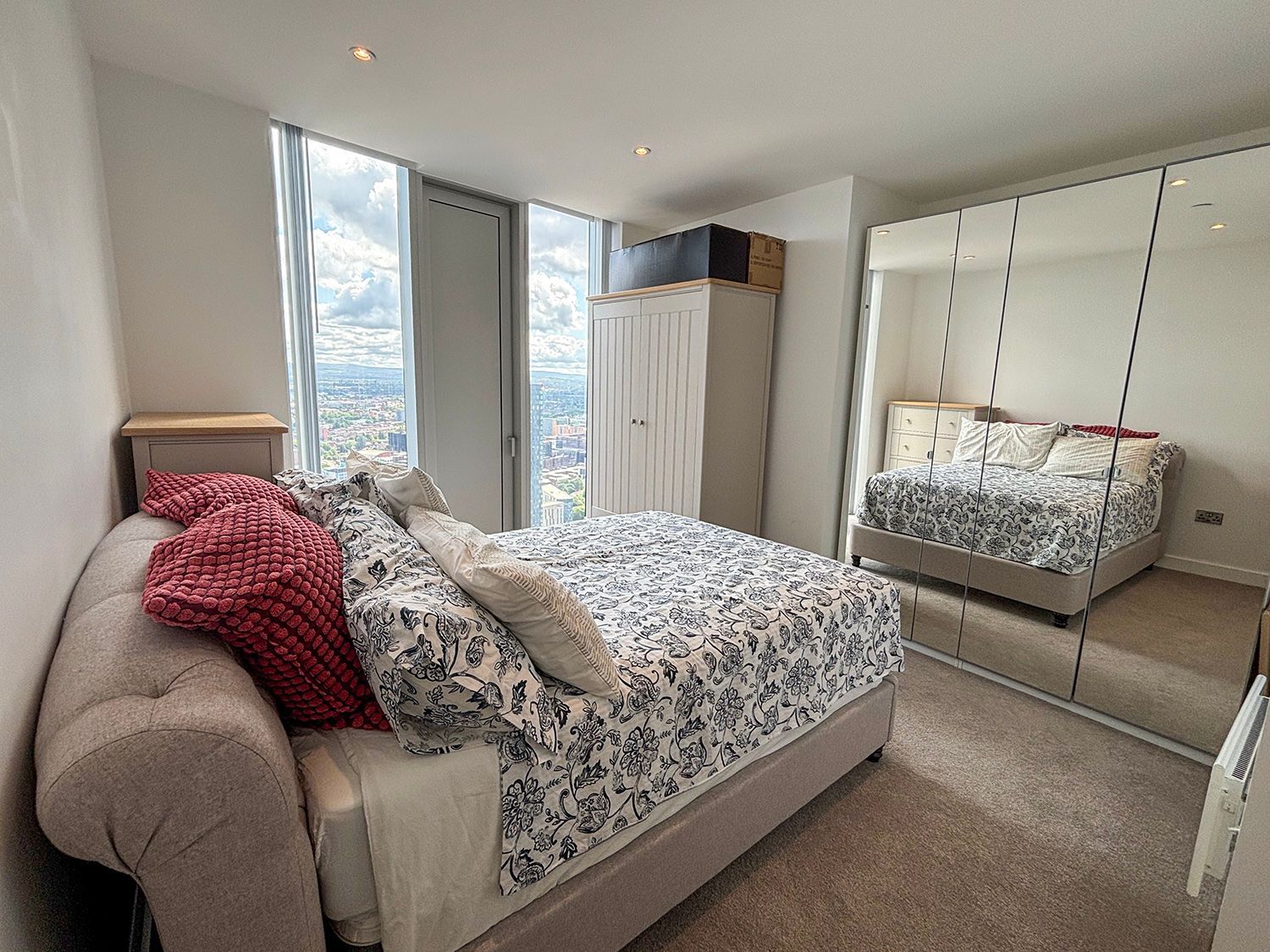 Bedroom with bed, mirrored closet, window, and cabinet. Neutral colors, natural light.