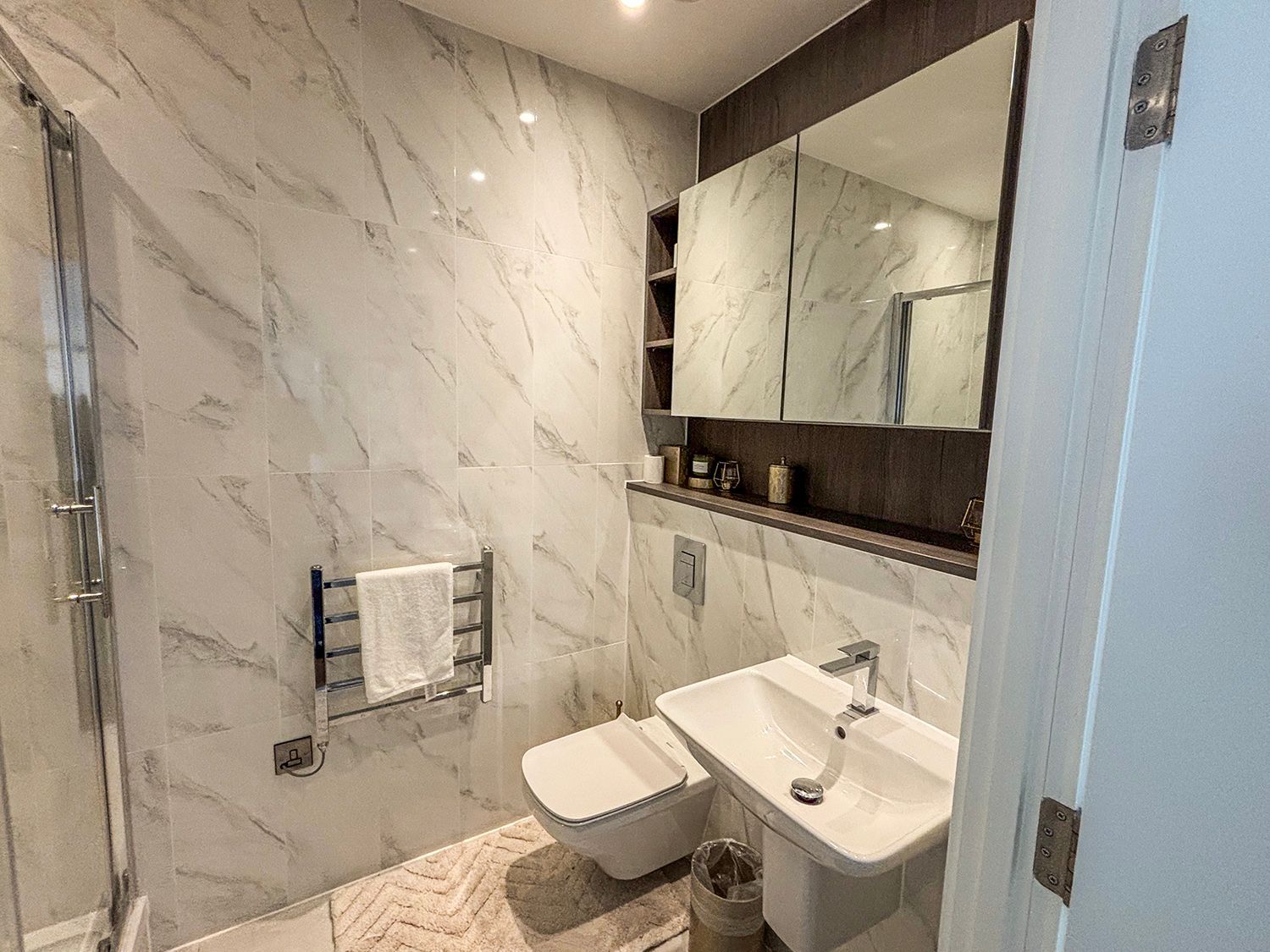 Modern bathroom with marble tile walls, a toilet, sink, and mirrored cabinet.