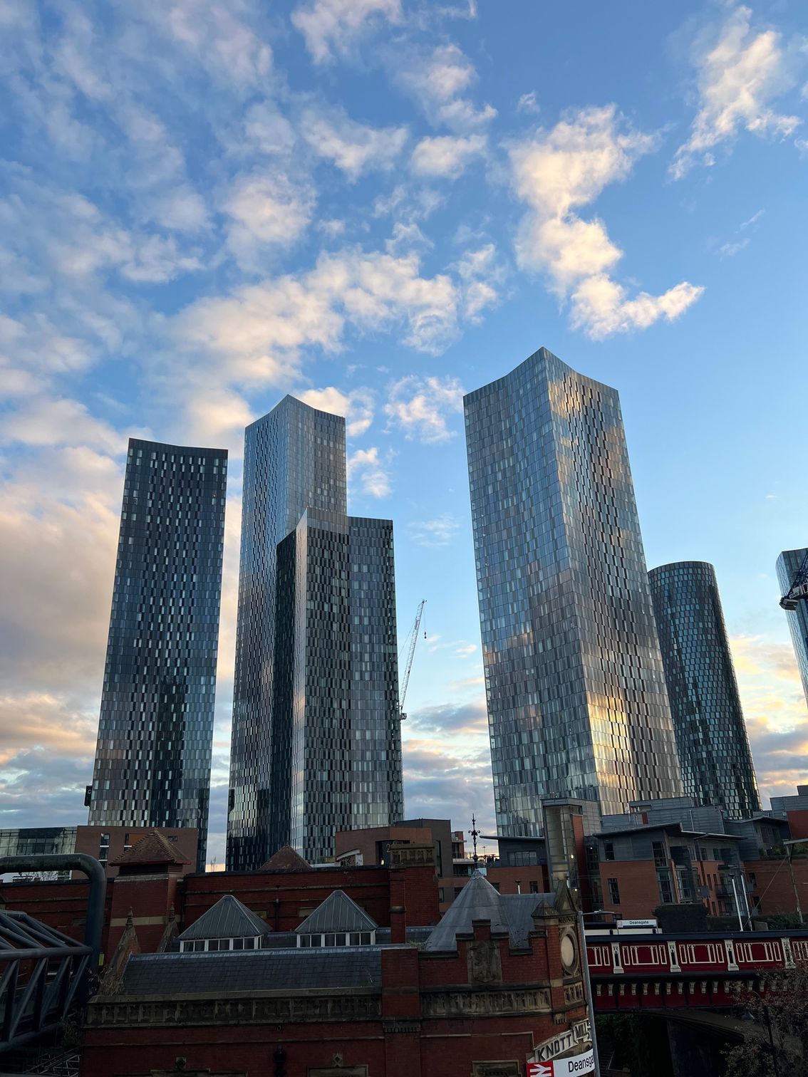 Skyscrapers rising above a red-brick building under a cloudy blue sky in an urban setting.