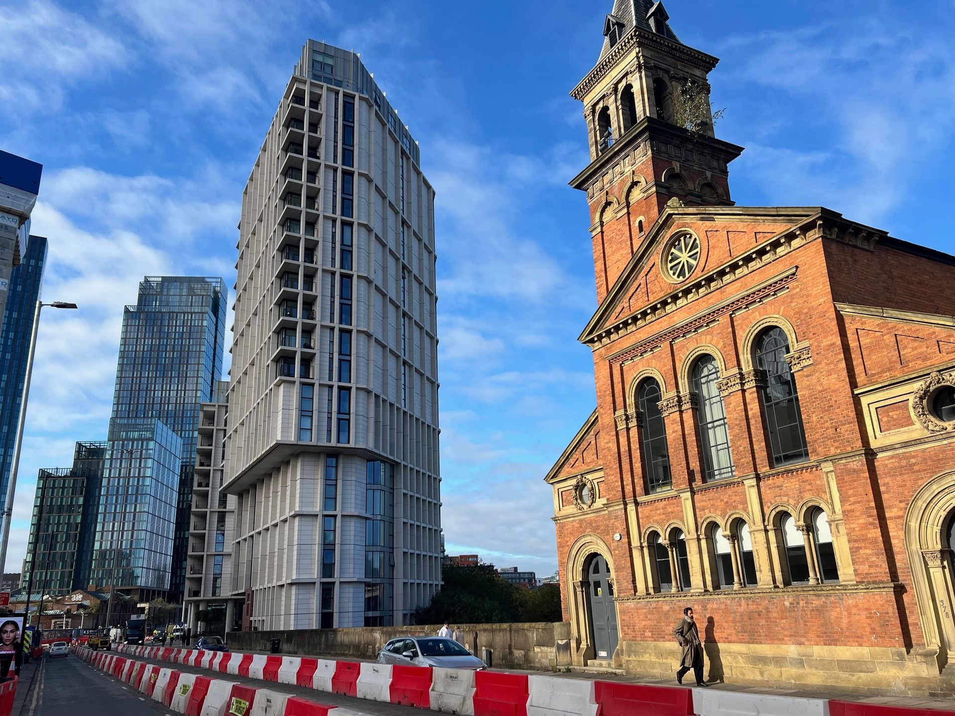 Modern buildings and a brick church against a blue sky, with a person walking.