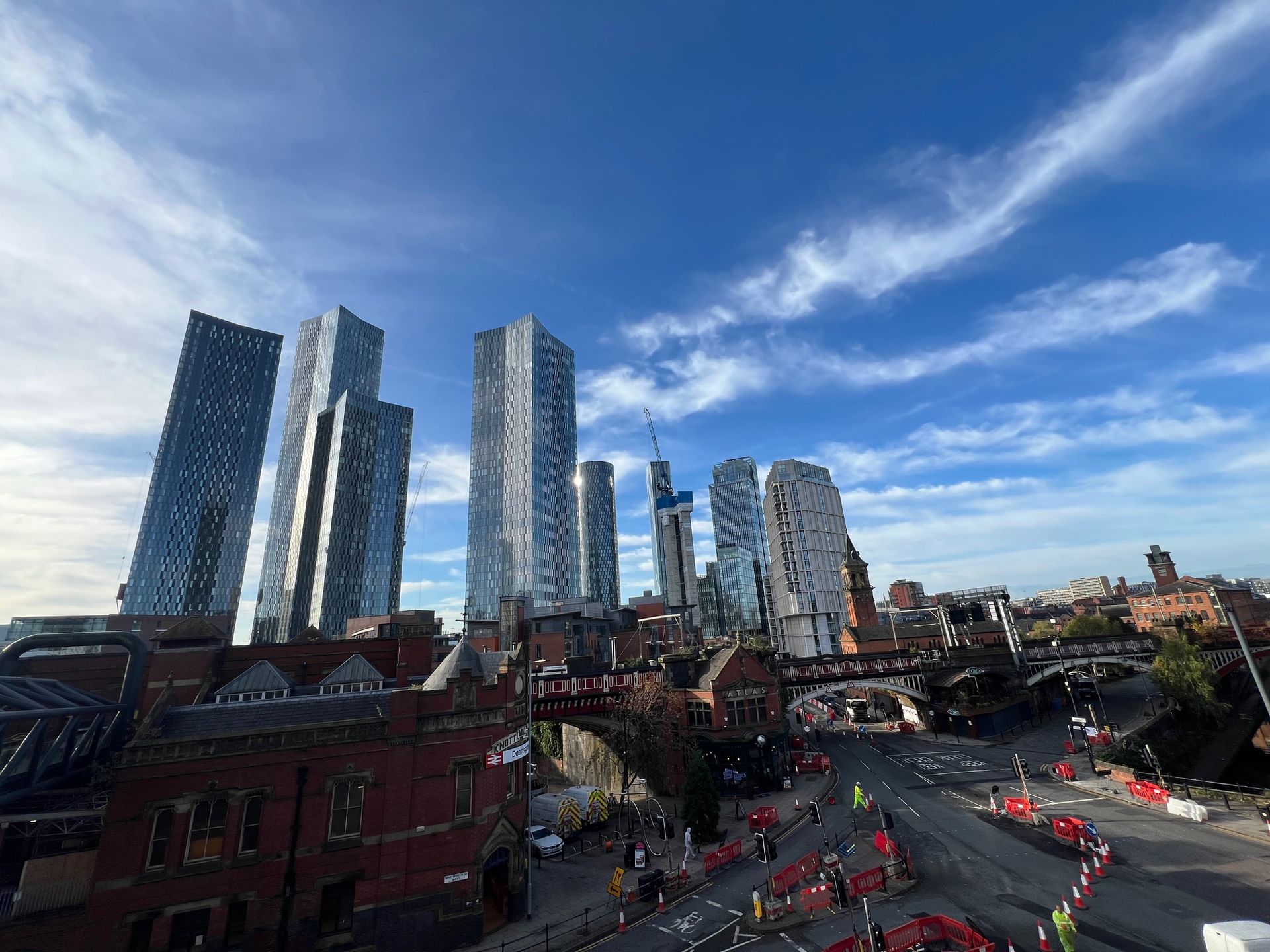 High-angle view of a city street with tall, modern skyscrapers against a blue sky with clouds.