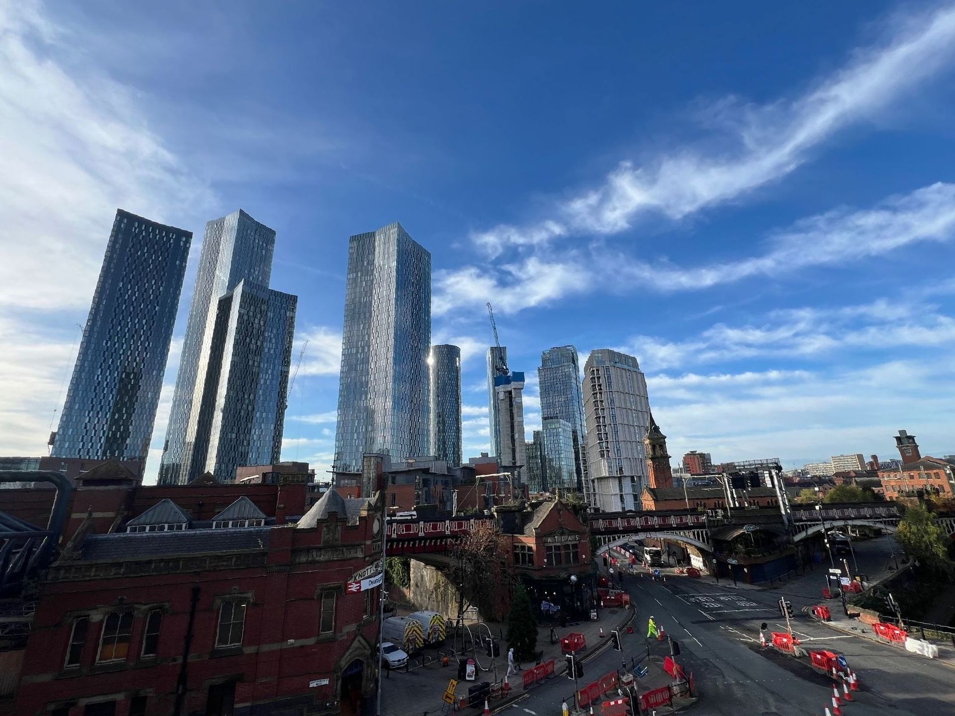 Skyscrapers over a city street with red barriers, under a blue sky with clouds.