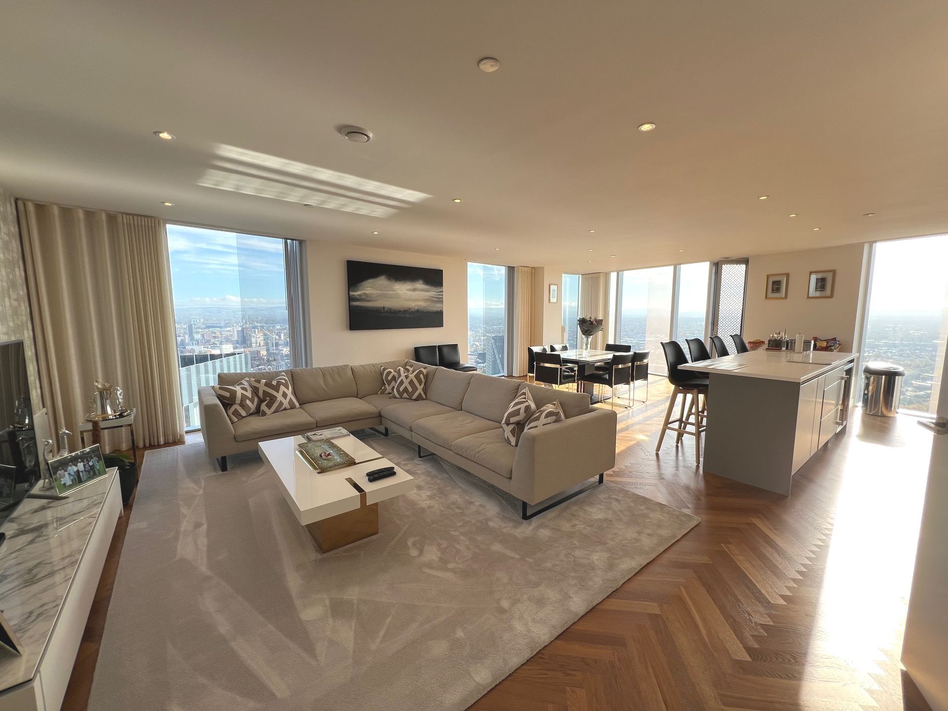 Spacious modern living room with city view, large windows, sectional sofa, and kitchen island.