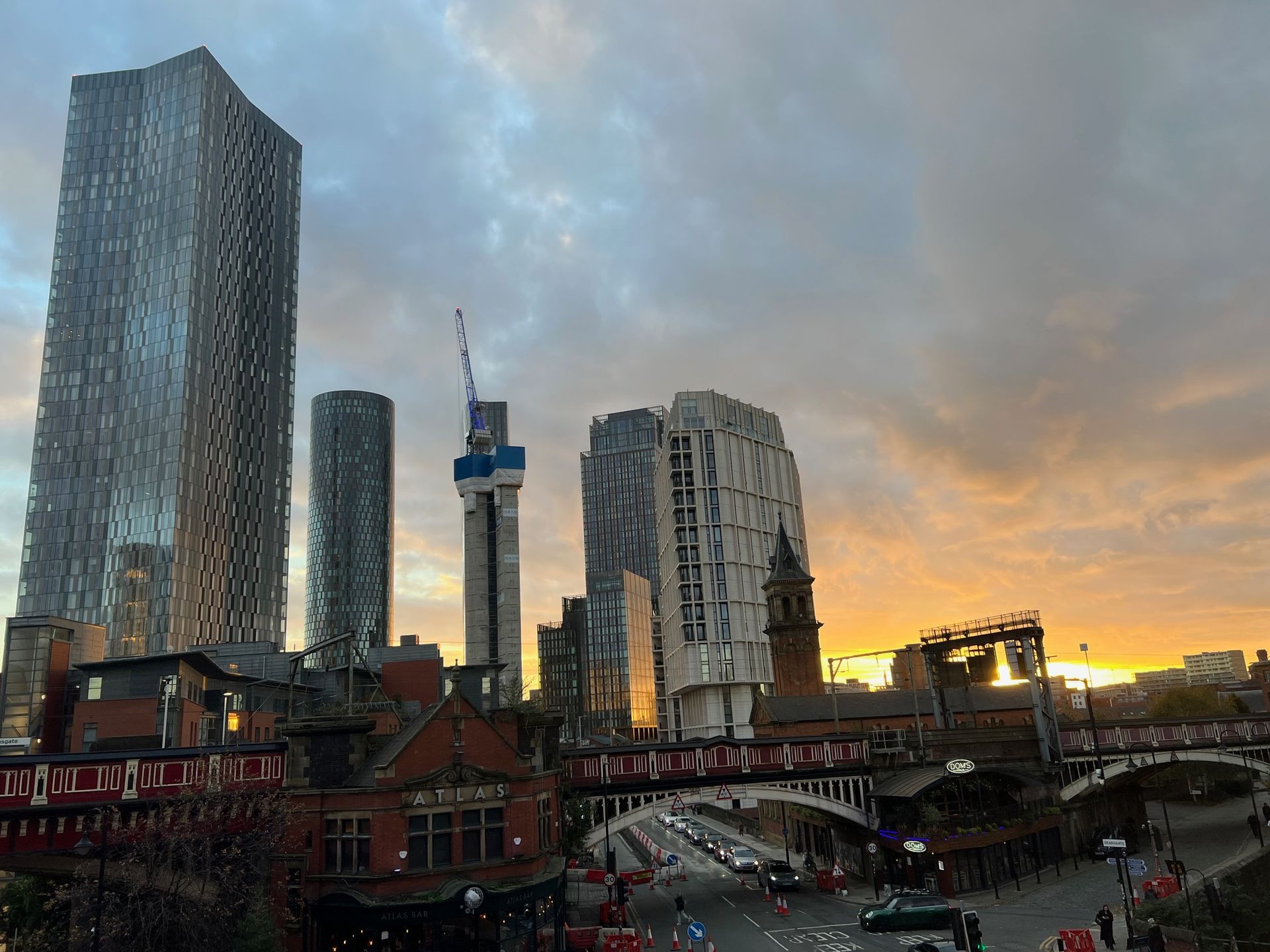 City skyline at sunset: skyscrapers, old buildings with brickwork, bridges, and orange-hued sky.