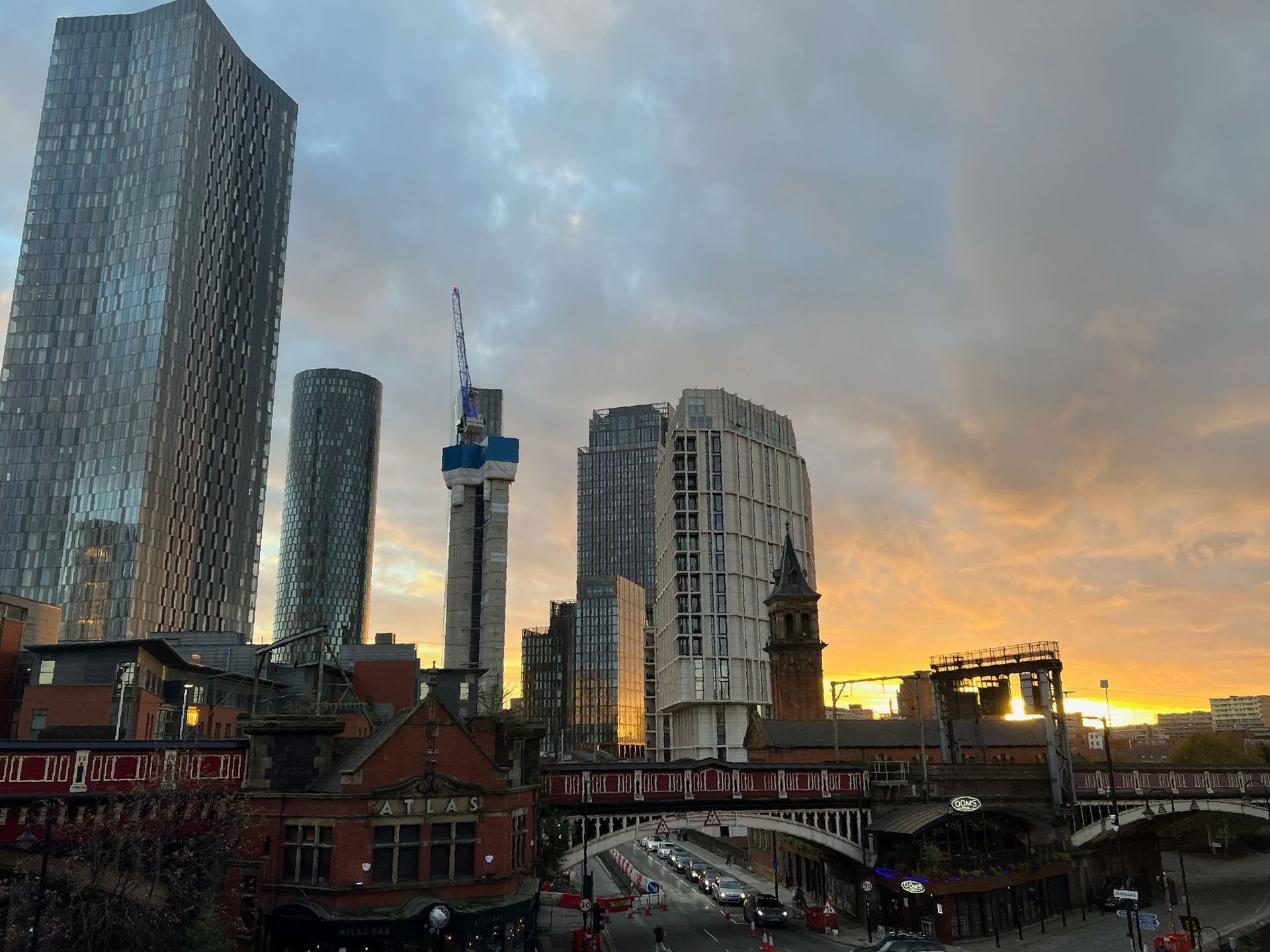 City skyline with skyscrapers, sunset sky, and a railway bridge.
