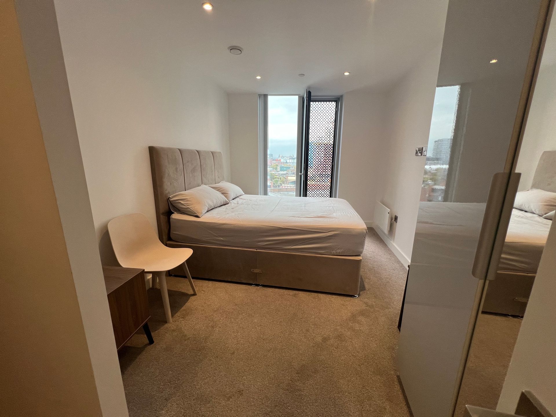 Bedroom with bed, nightstand, chair, and large window with city view.
