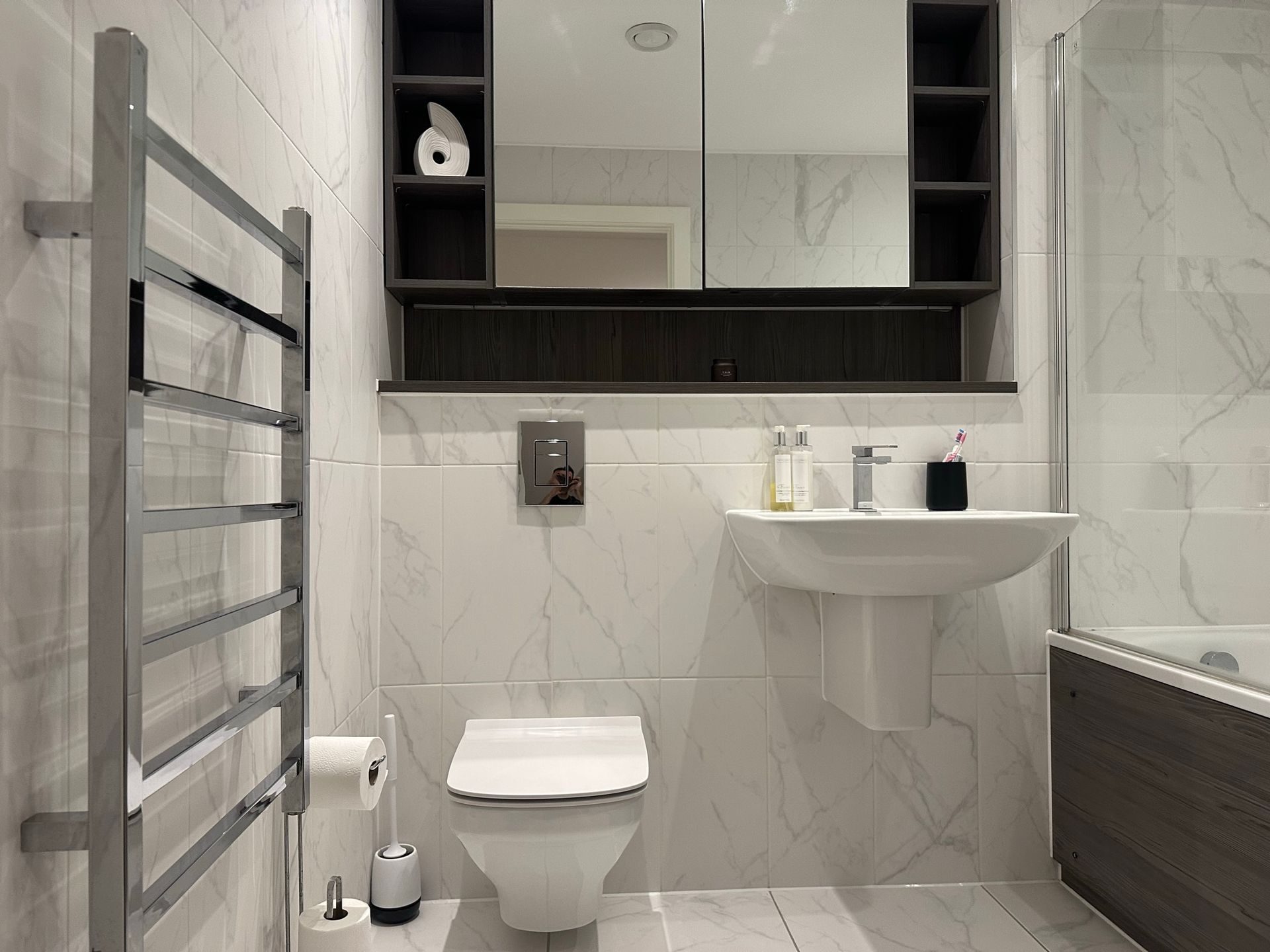 Modern bathroom with white and gray tiled walls, toilet, sink, mirror cabinet, and towel rack.