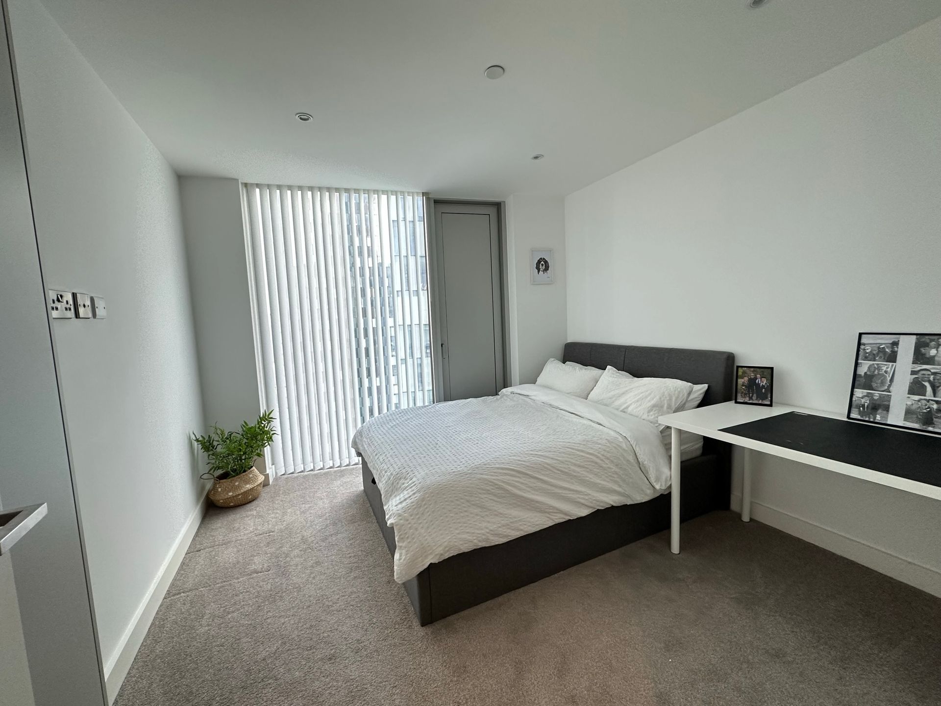 Bedroom with bed, desk, and window with blinds. Neutral colors and natural light.