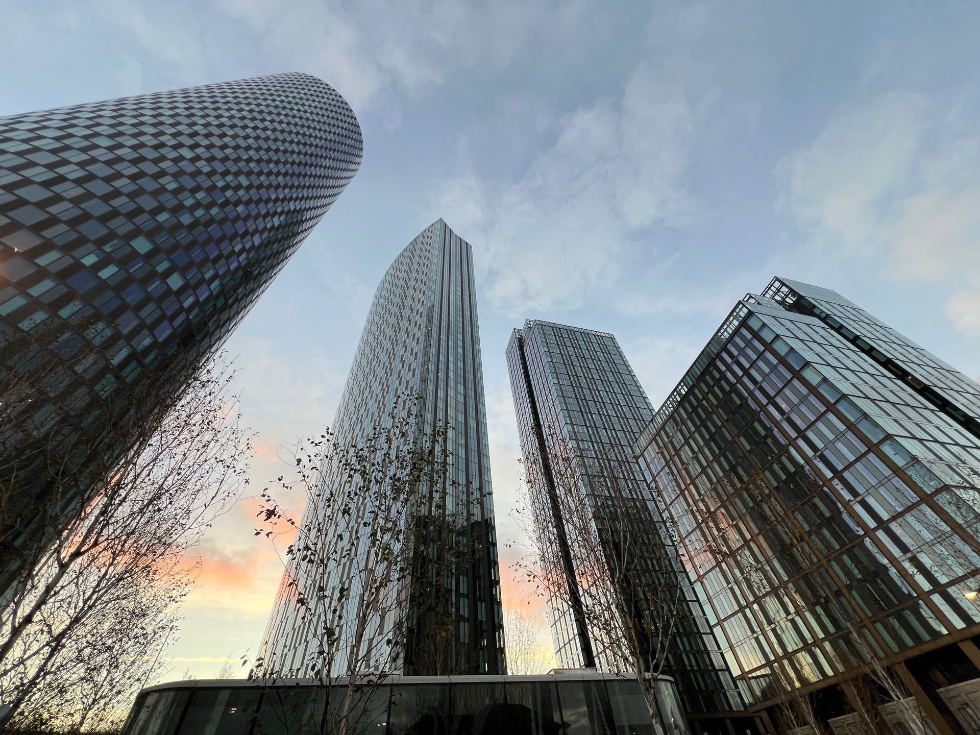 Four modern skyscrapers reaching towards a cloudy sky at sunset.