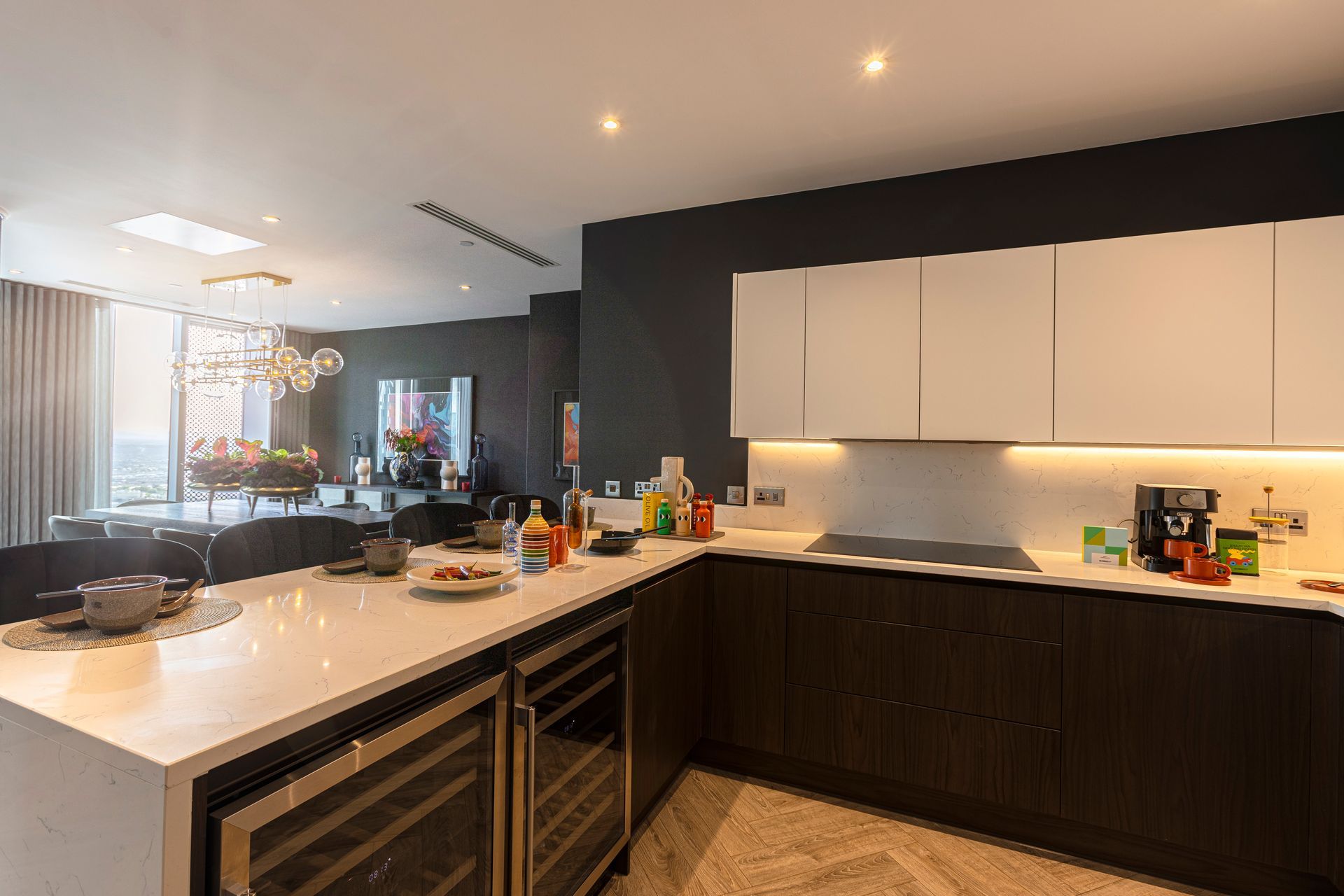 Modern kitchen with white countertops and dark cabinets; open to a dining area.