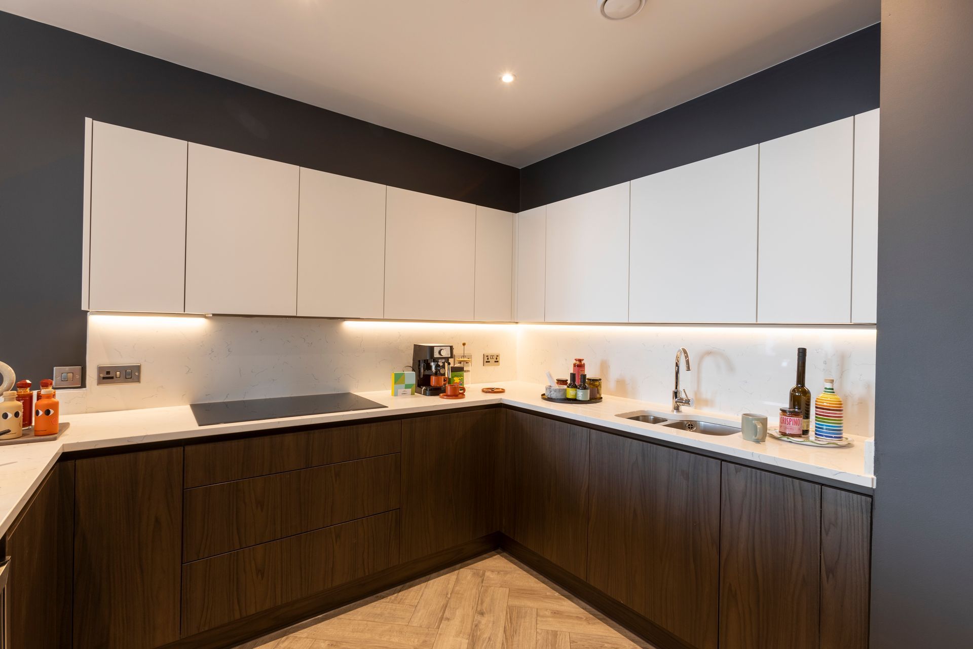 Modern kitchen with white and dark wood cabinets, white countertops, and dark gray walls.