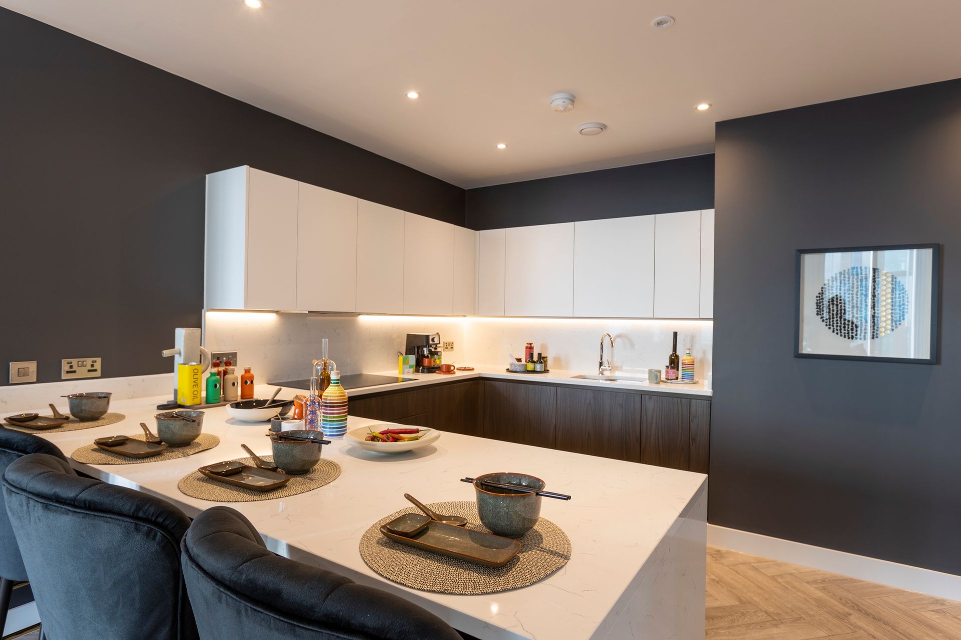 Modern kitchen with white countertops and cabinets, dark gray walls, and an island with bar stools.
