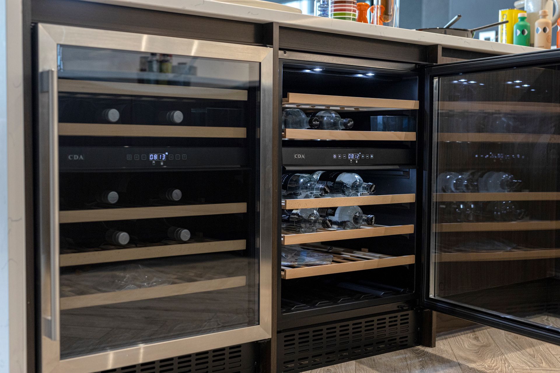 Two built-in wine refrigerators, one closed, one open, displaying bottles and glassware on wooden racks.