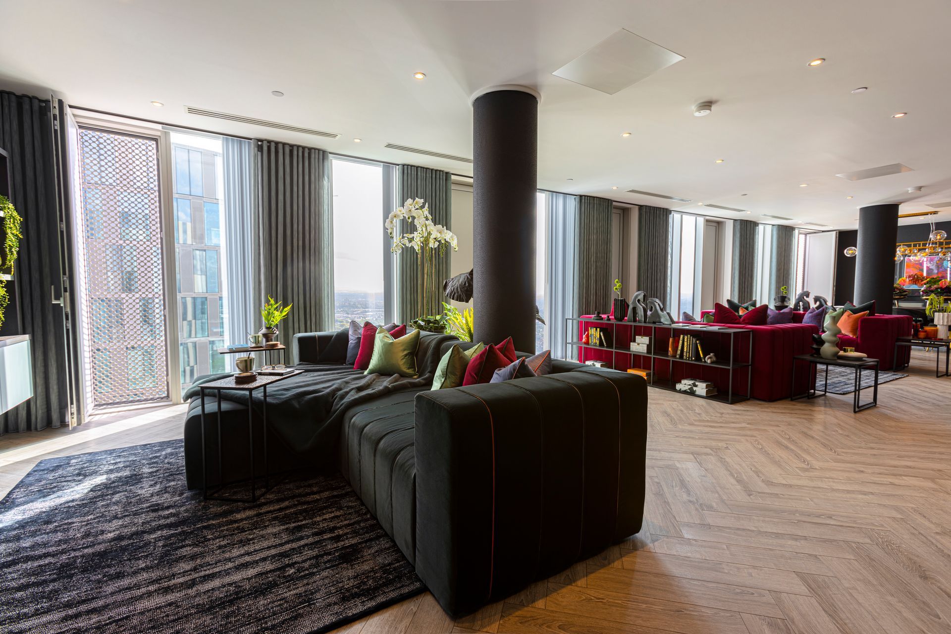 Modern living room with black sectional sofa, large windows, and a circular red couch.