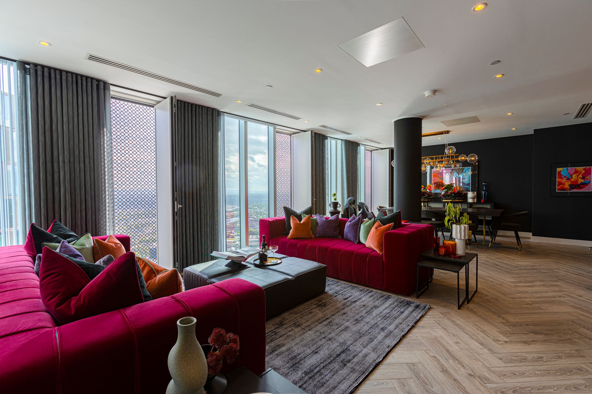 Modern living room with magenta sofa, large windows, and city view.