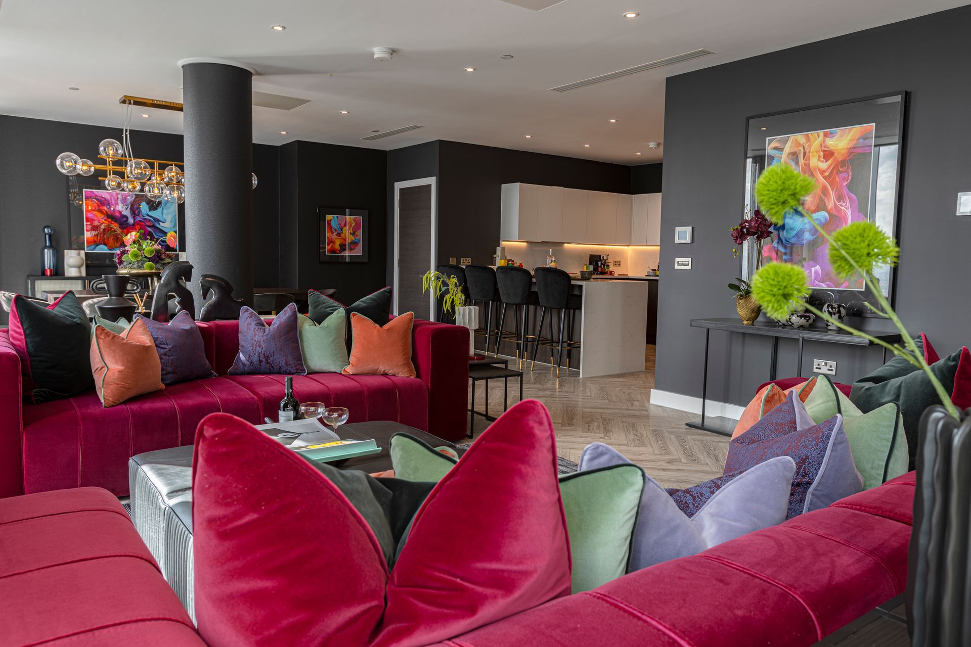 Luxurious living room with red sofa, colorful pillows, and open kitchen with a bar.