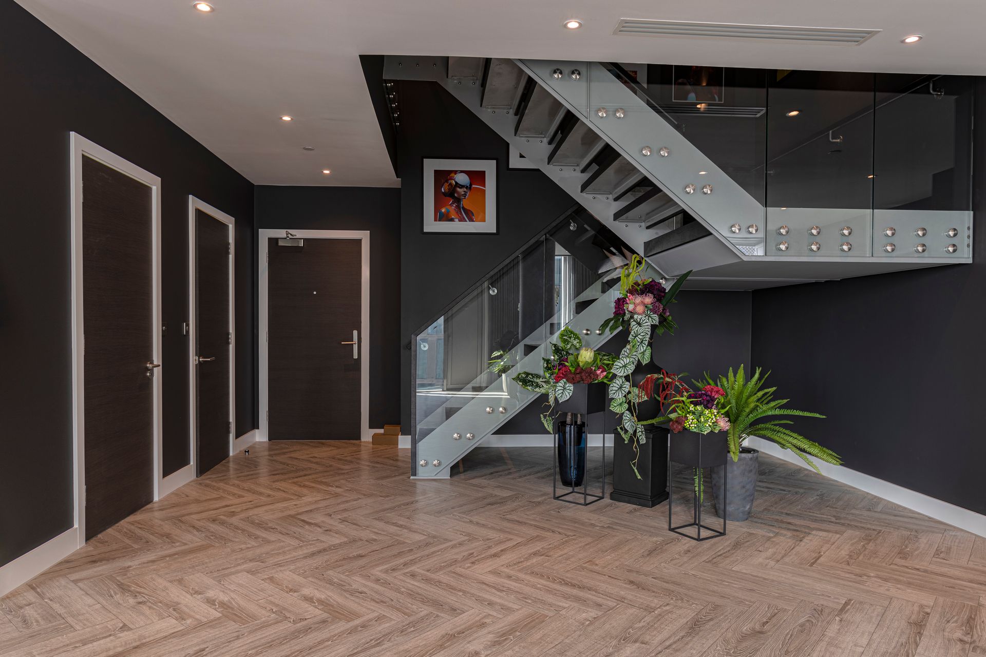 Hallway with stairs and modern decor: dark walls, patterned floor, floral arrangements, metal staircase.