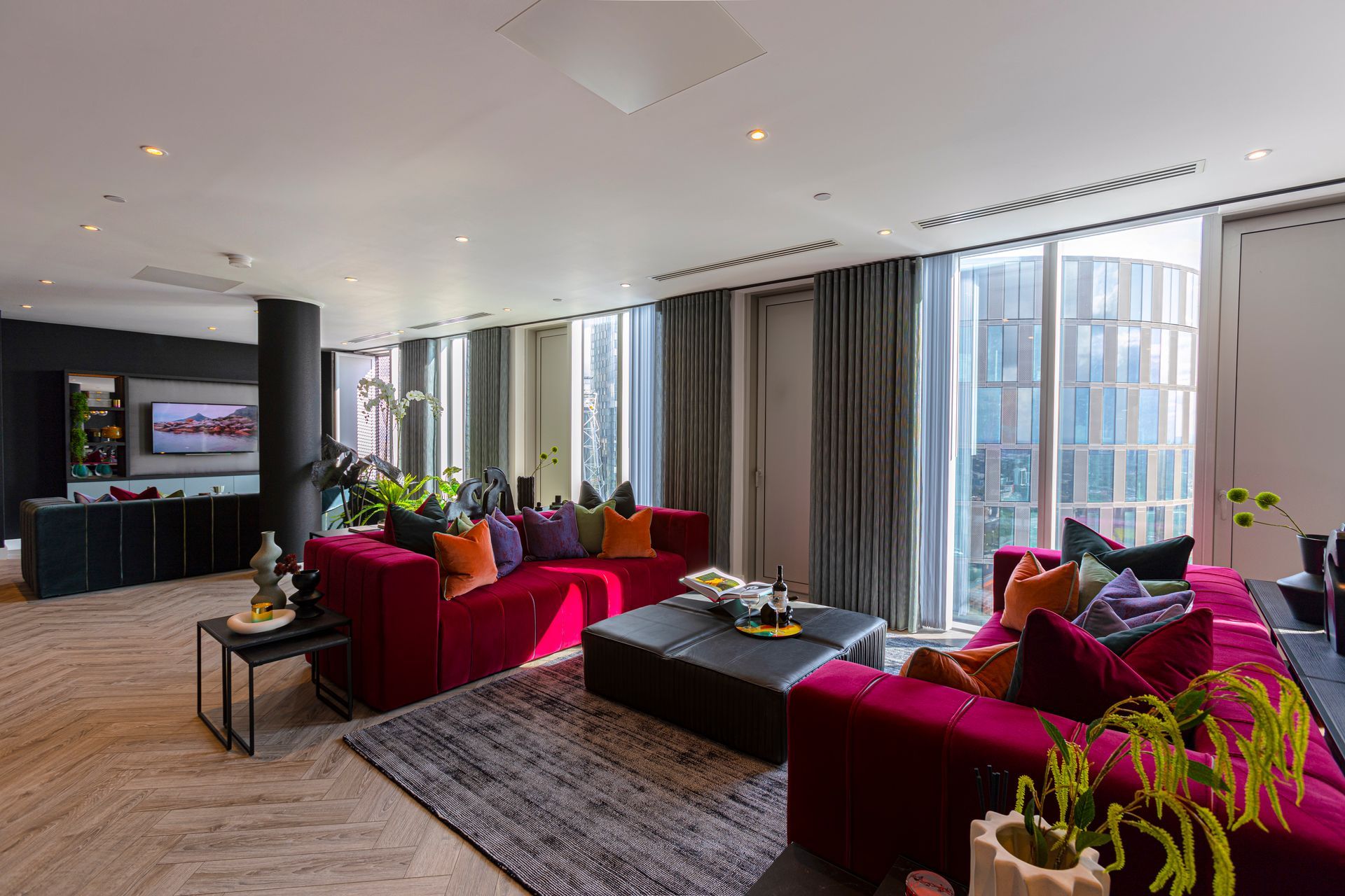 Spacious, modern living room with red sofas, large windows, and city views.
