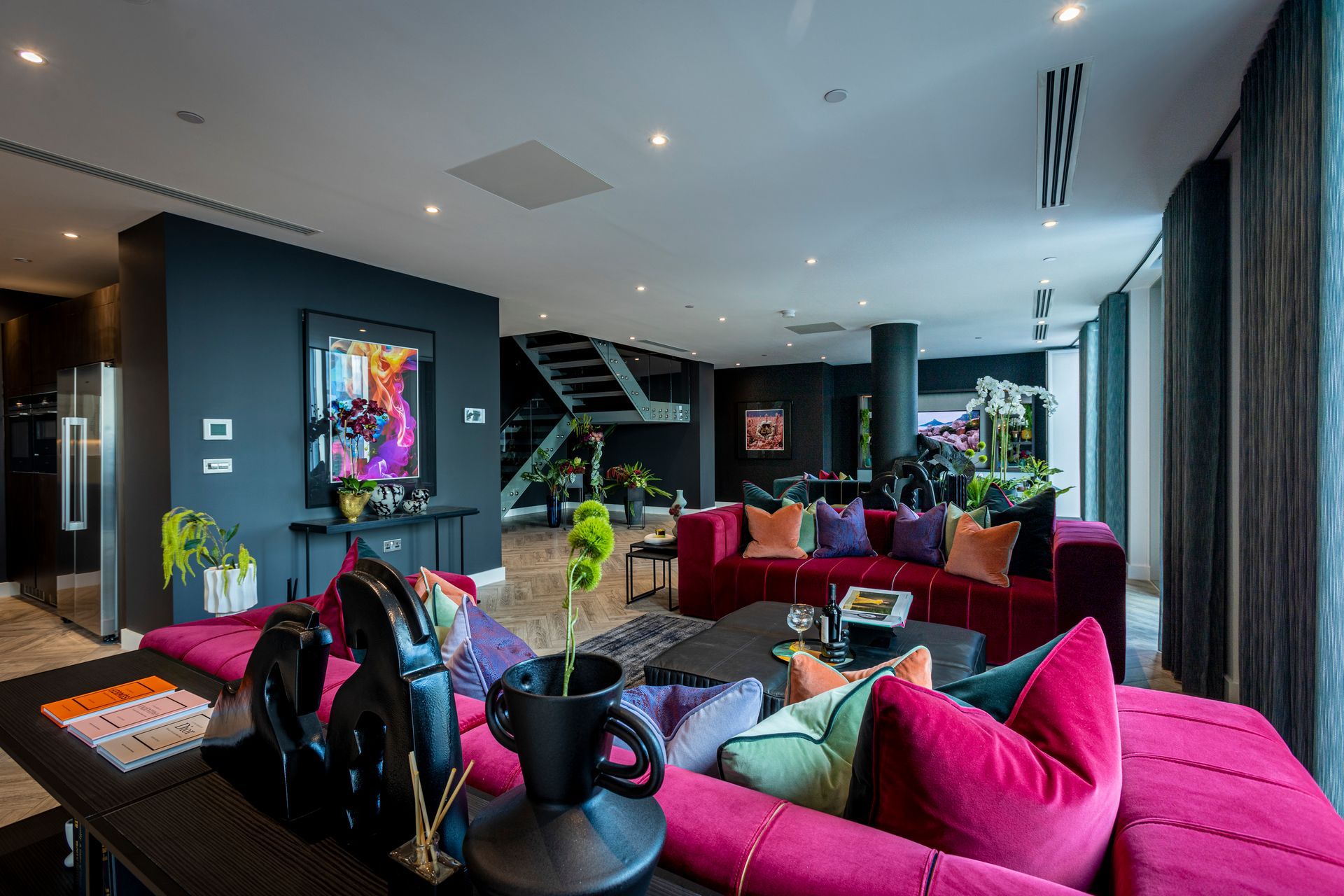 Spacious, modern living room with magenta sofa, dark blue walls, art, and curved windows.