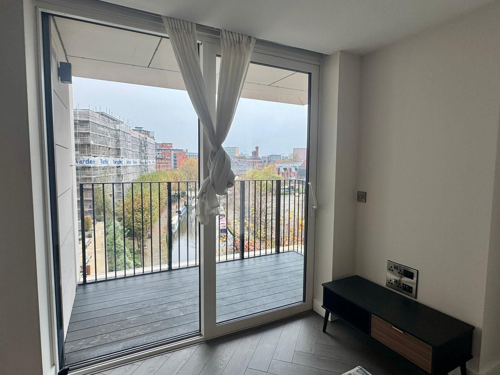 Interior view of a modern apartment with a balcony. Glass doors, dark gray floor, black TV stand, light curtains.