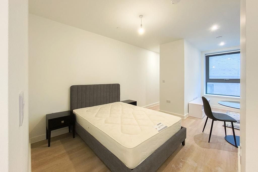 Bedroom with bed, nightstands, chair, and desk by a window. White walls, wood floor.
